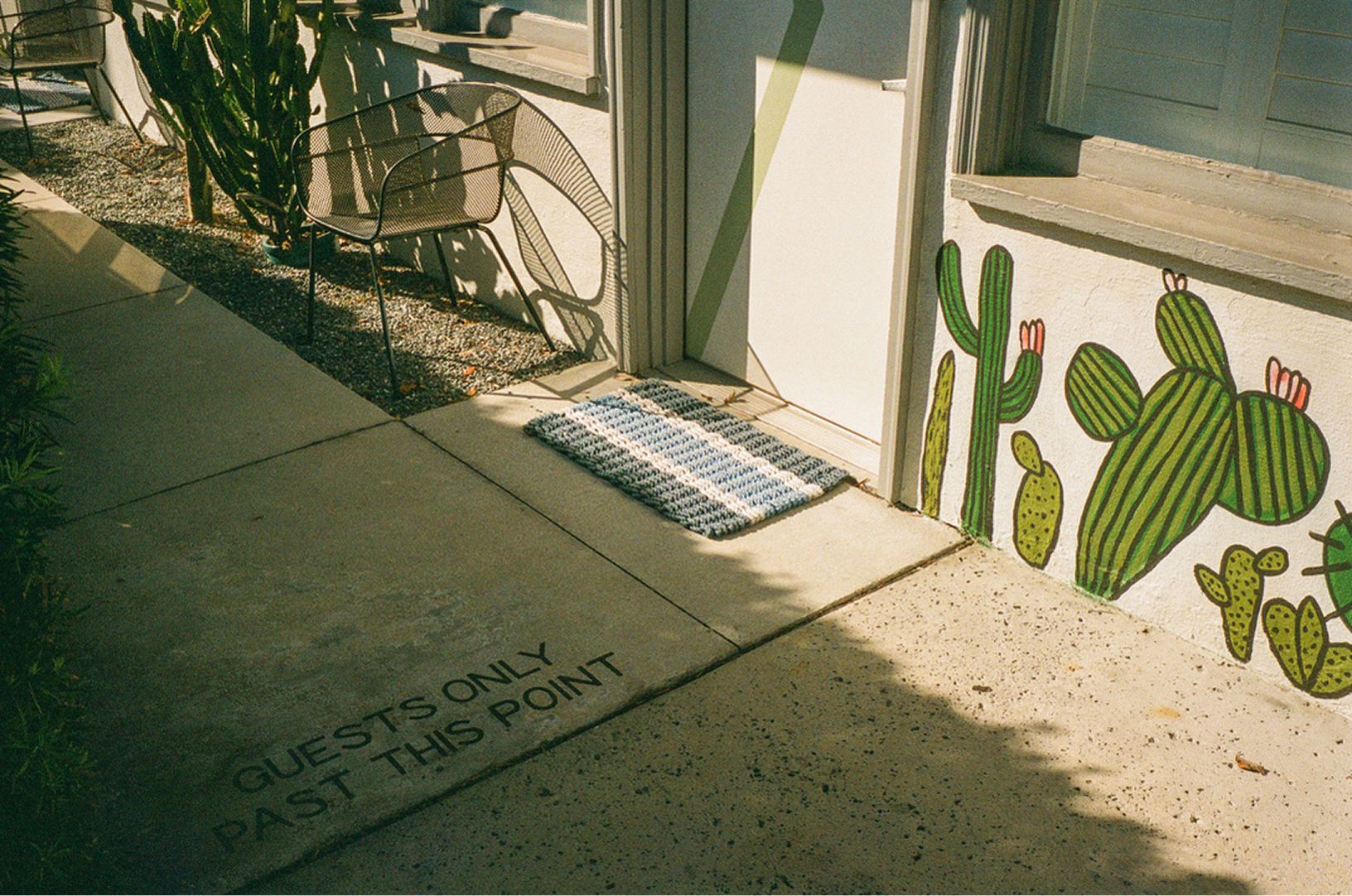 Sunlit sidewalk outside a cactus-themed storefront with a doormat by the door