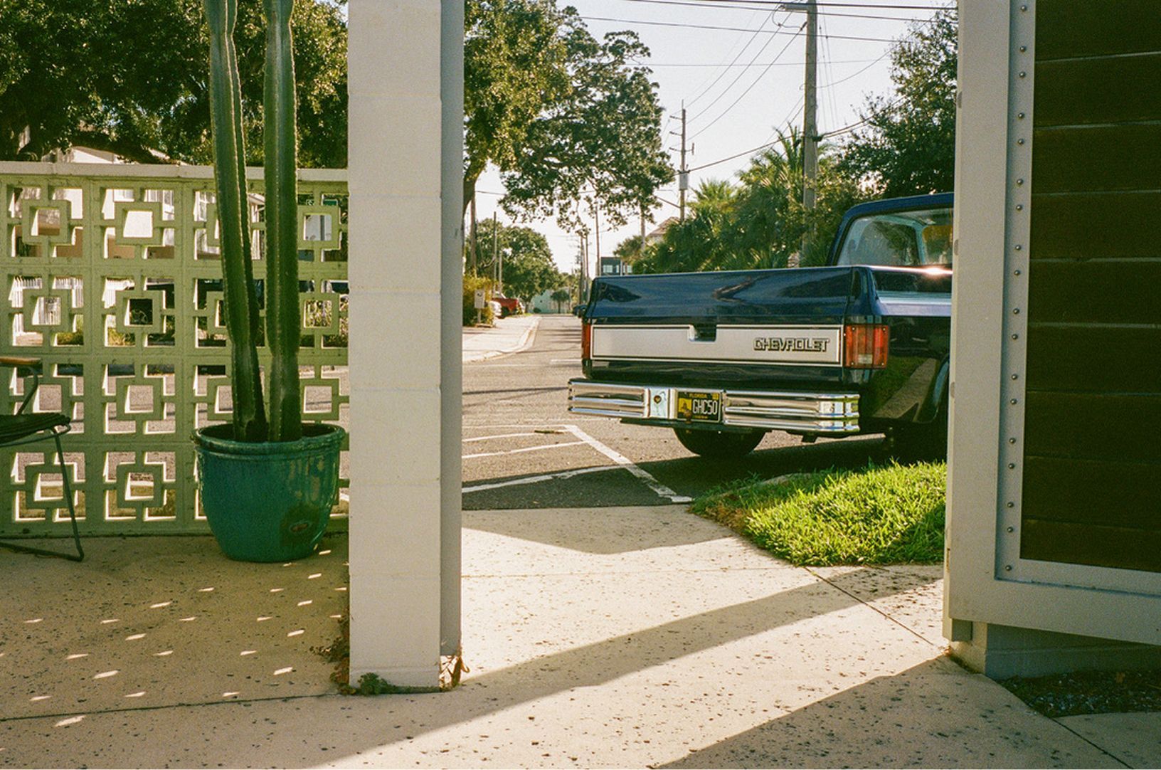 Blue pickup truck parked in a sunlit driveway beside a house and white column