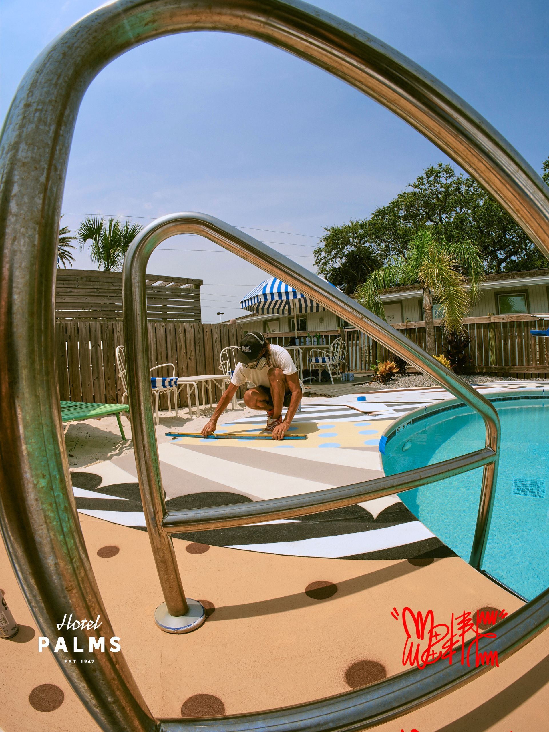 Person lounging on a poolside deck by a turquoise pool, framed by curved metal rails under a blue sky