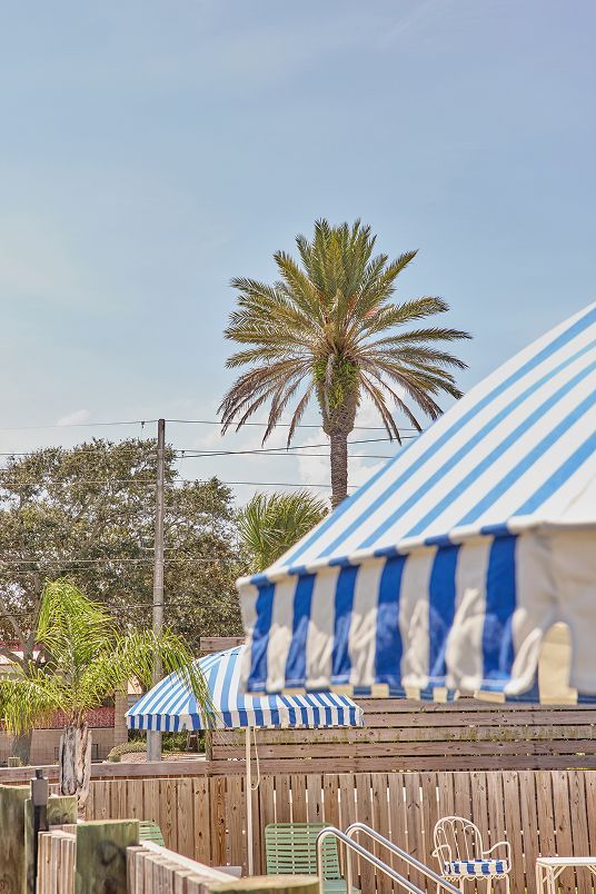 Blue-and-white striped tent with palm trees and a wooden fence at an outdoor fairground