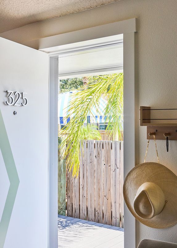 Open doorway with house number 325, showing a sunlit patio, fence, and palm fronds outside