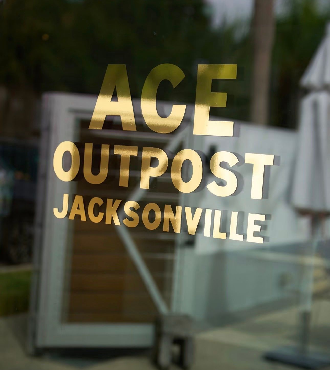 Gold “ACE OUTPOST JACKSONVILLE” lettering on a glass door, with a blurred outdoor background