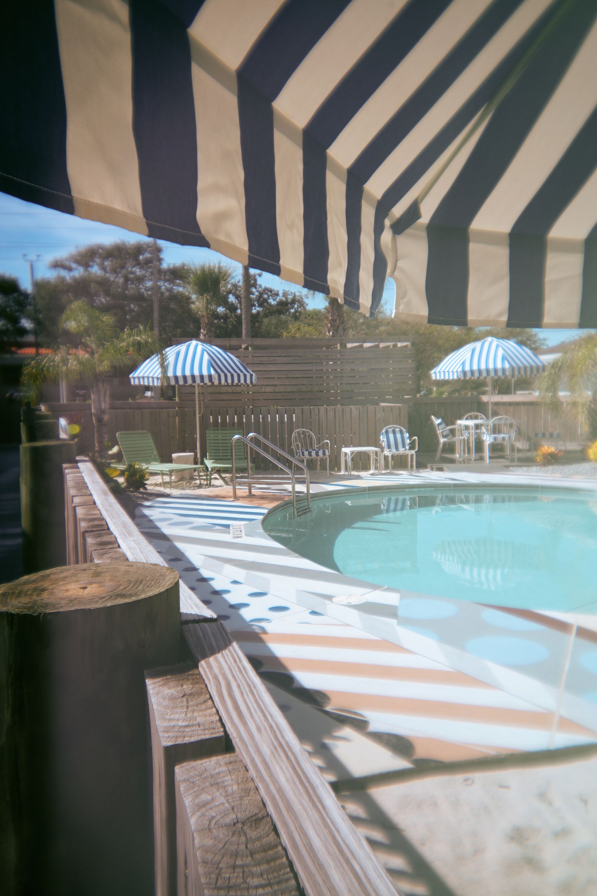 Shaded poolside patio with striped awning, lounge chairs, and a turquoise swimming pool.