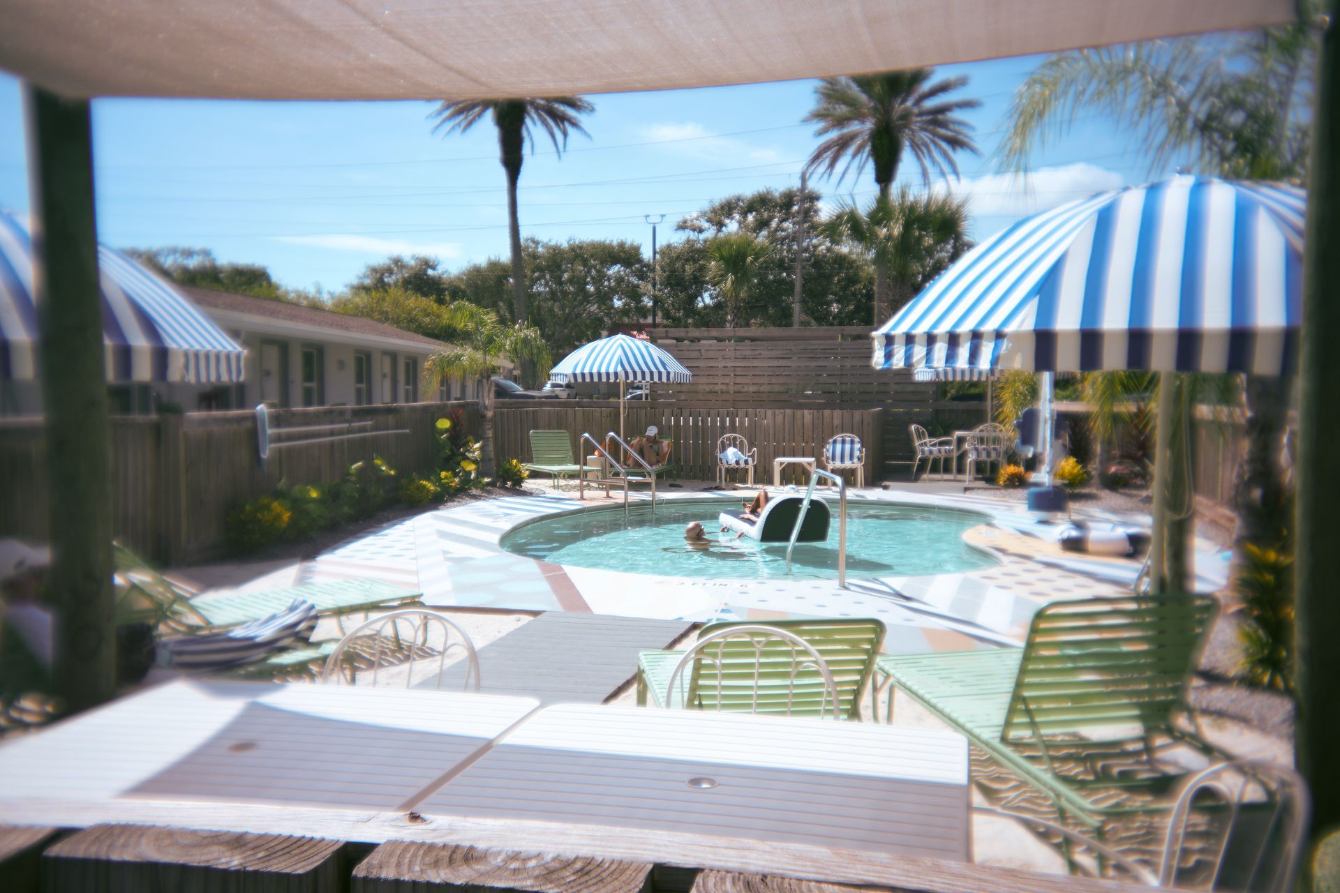 Resort-style pool with lounge chairs, striped umbrellas, and a water fountain under a shaded patio