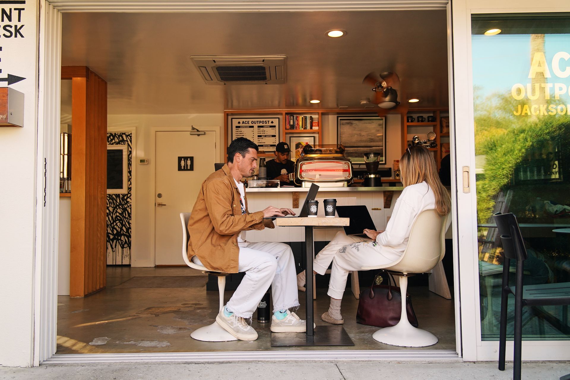 Two people sitting at a café table, talking in a bright storefront interior