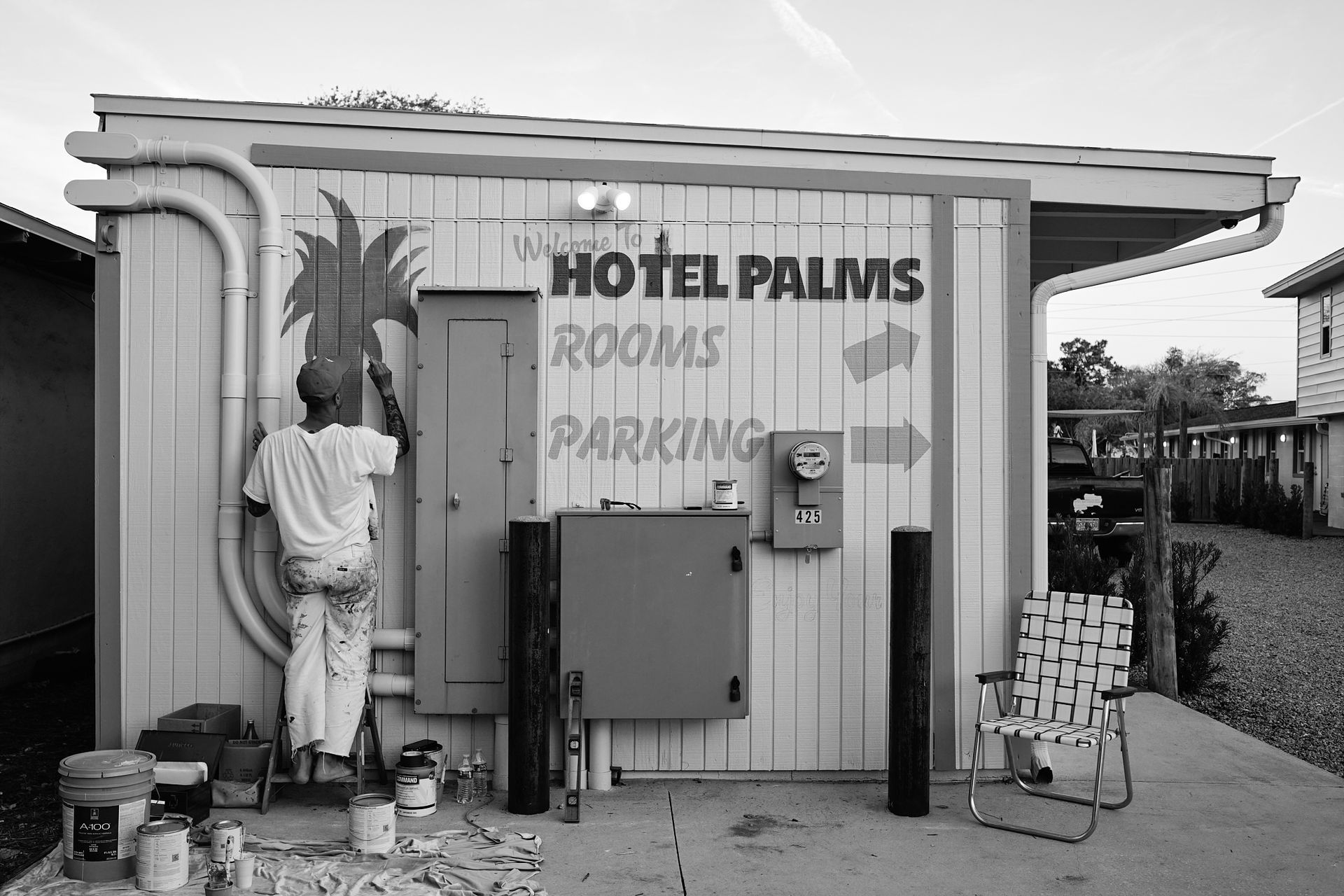Small roadside hotel entrance with “Hotel Palms” sign, a statue, and parked luggage carts.