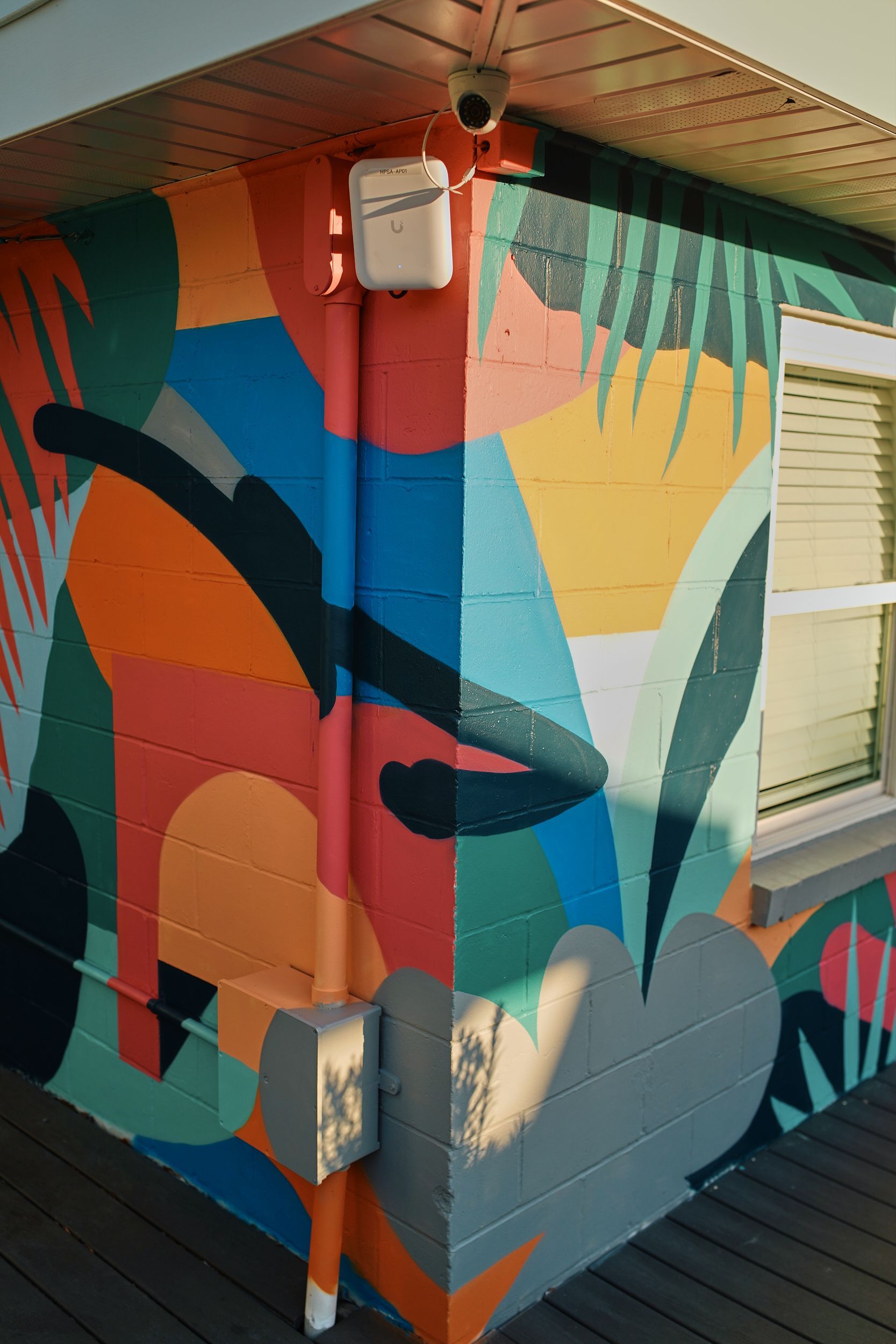 Colorful abstract mural on the corner of a building beside a window and deck.