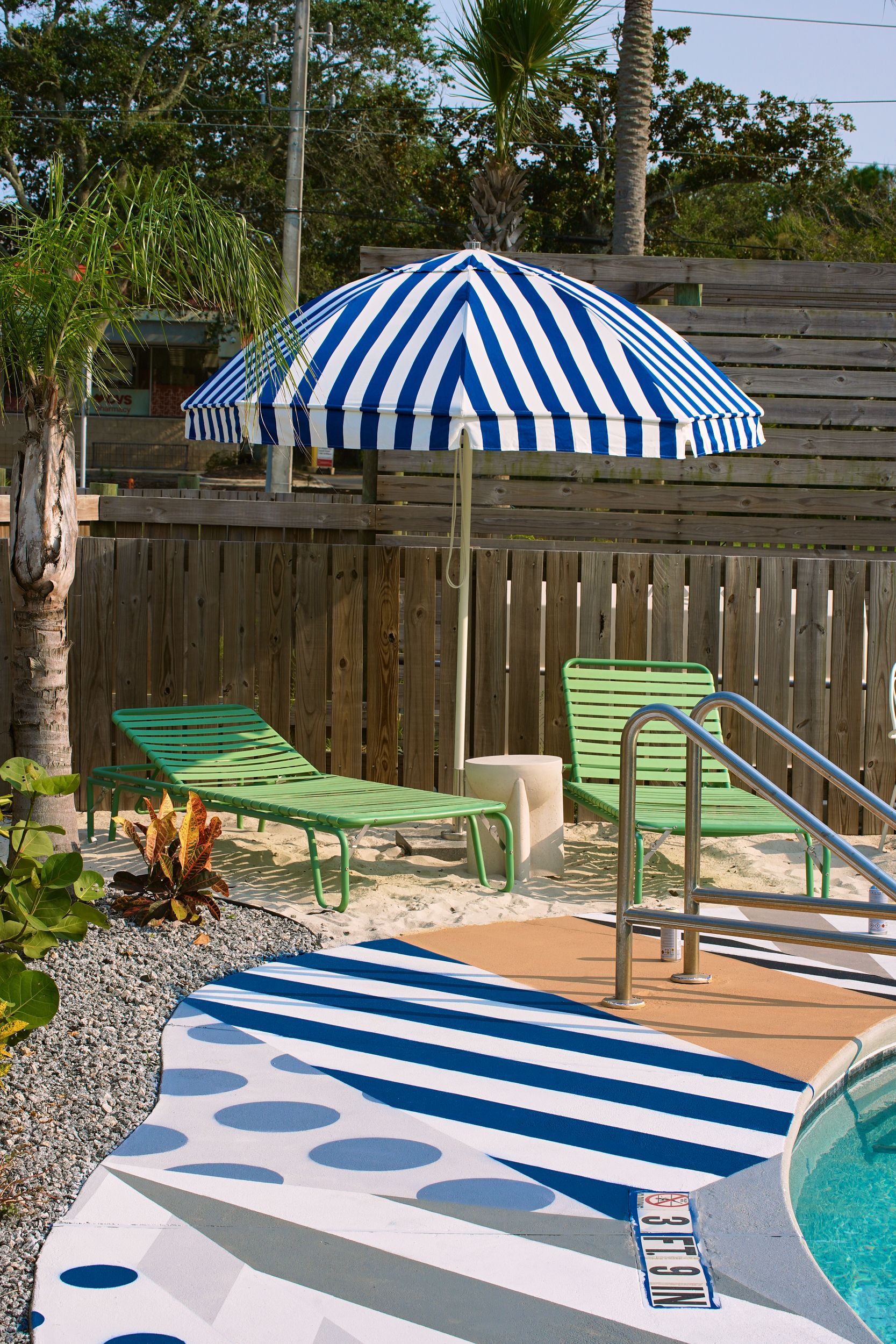 Blue-and-white striped pool umbrella beside lounge chairs and a swimming pool in a backyard patio area