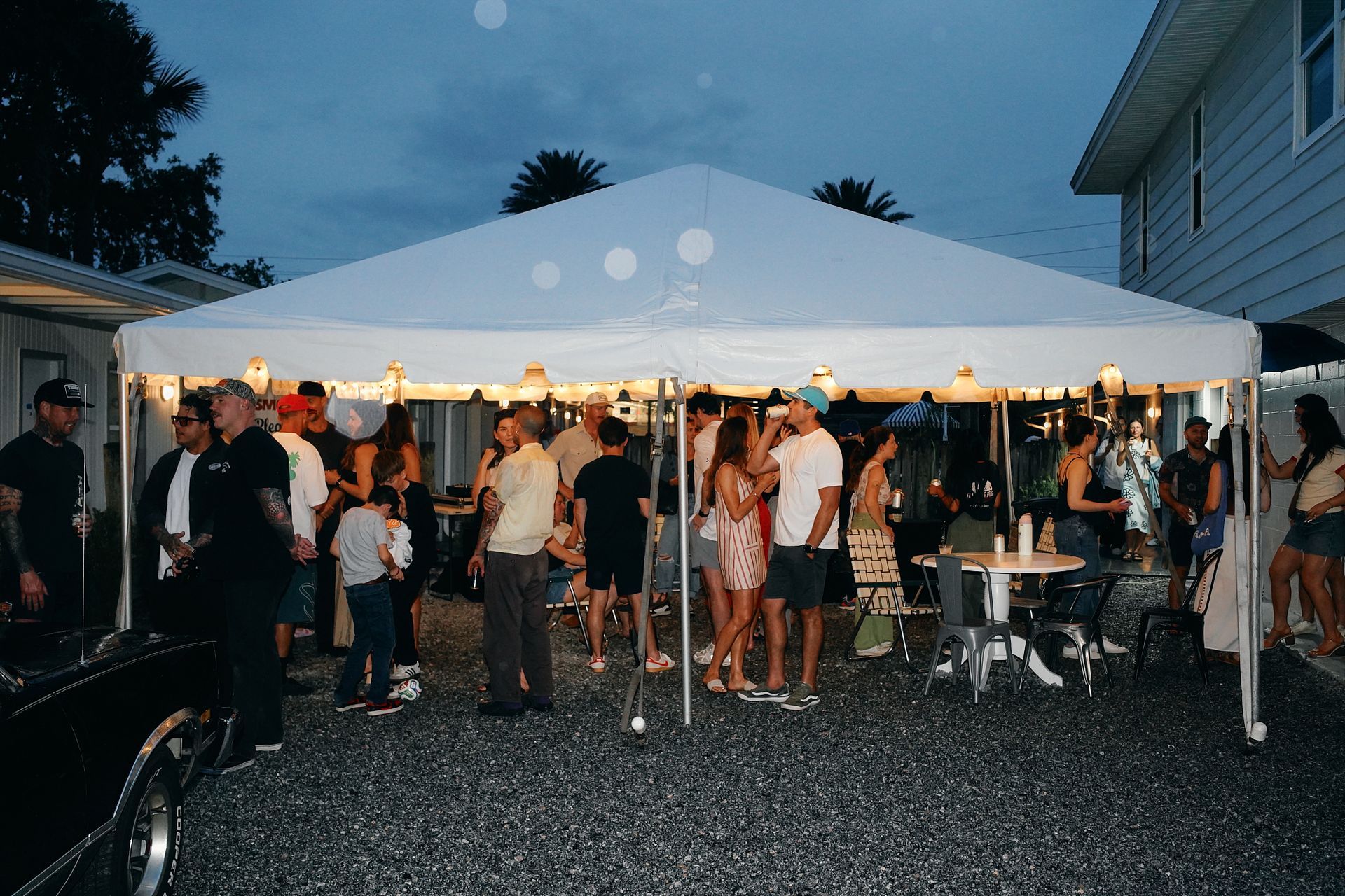 People mingling under a white canopy tent at an outdoor evening gathering