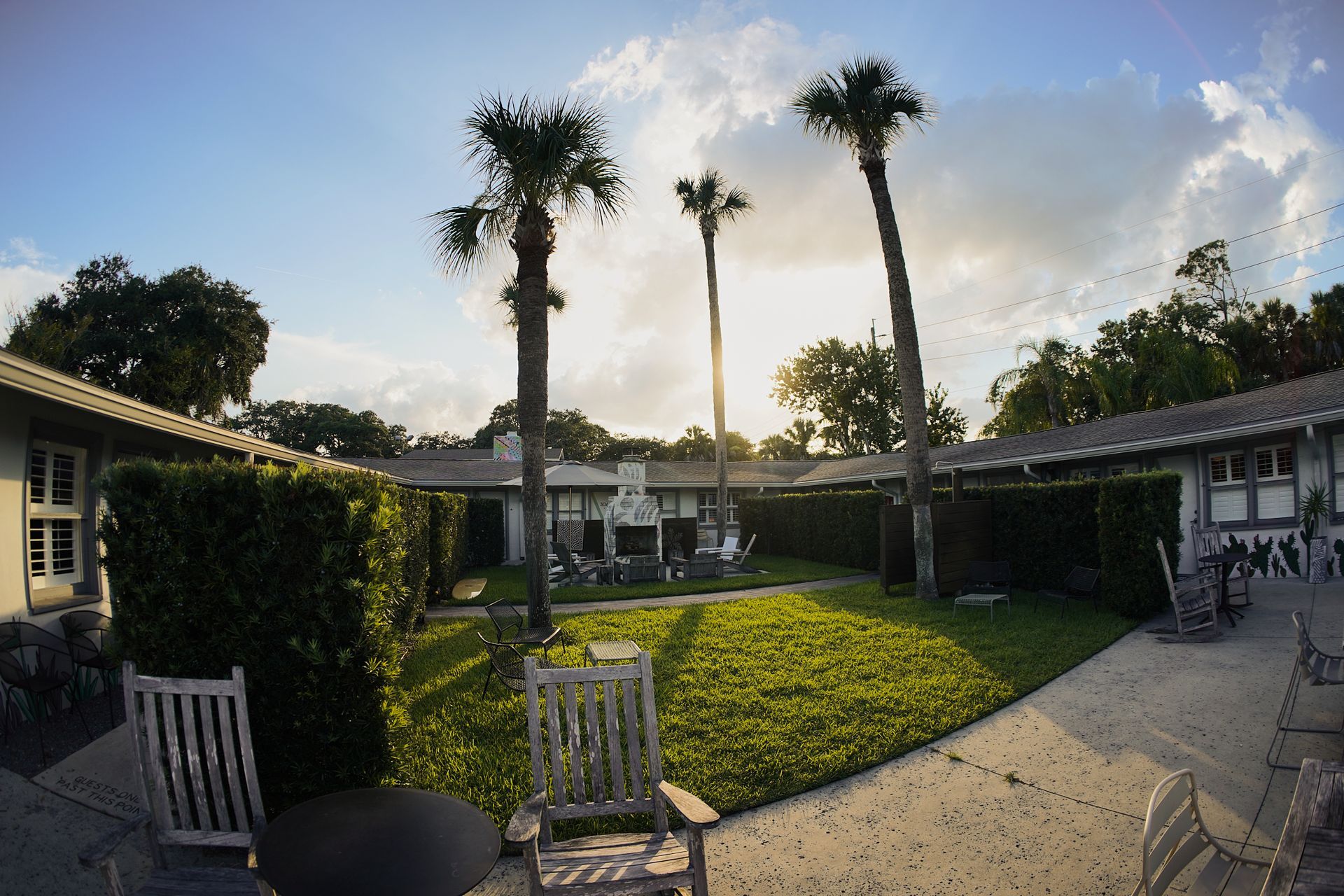 Courtyard with palm trees, green lawn, and patio chairs beside low buildings at sunset