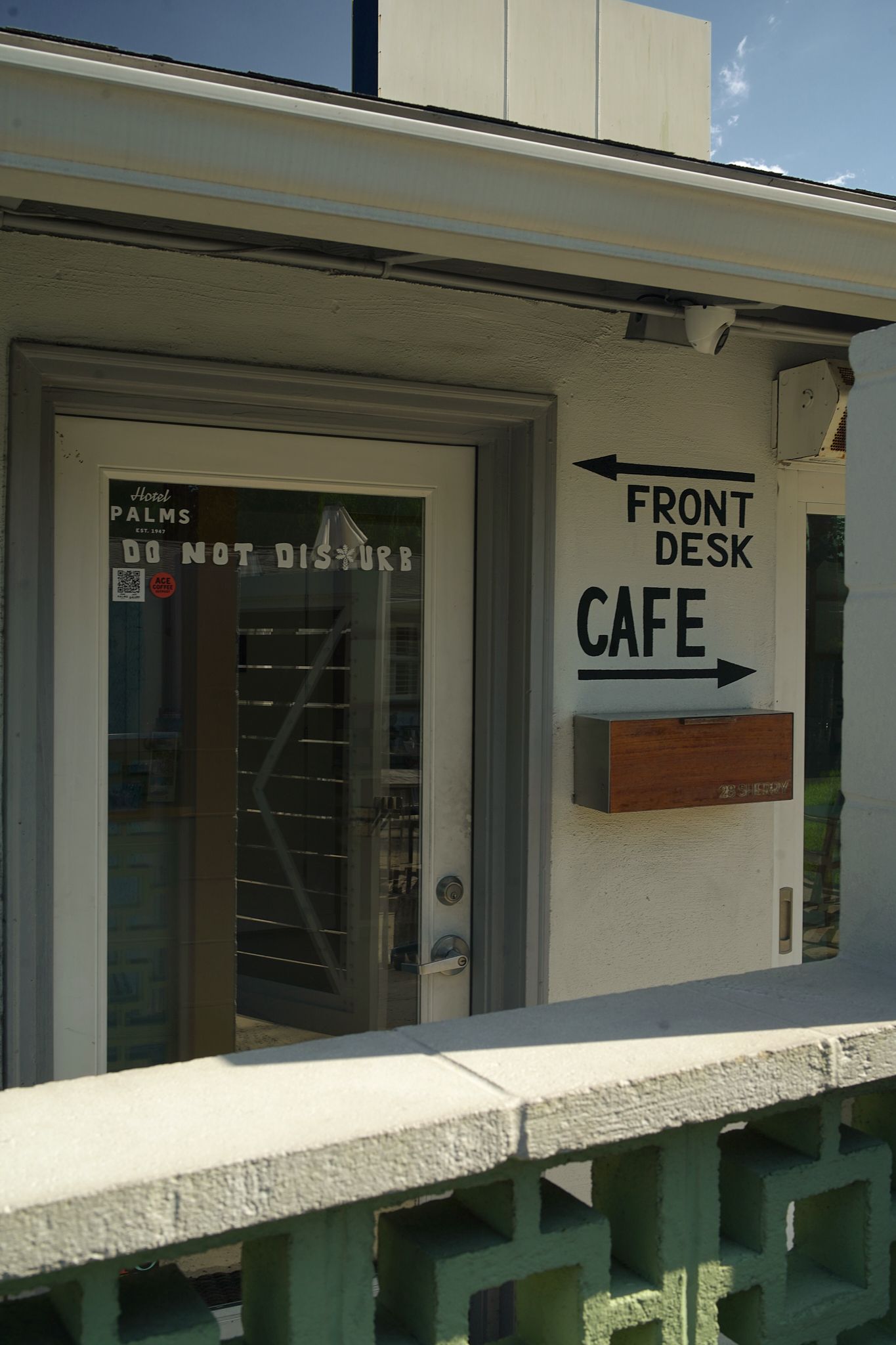 Front desk and cafe sign beside a doorway on a beige building, with a railing in front.