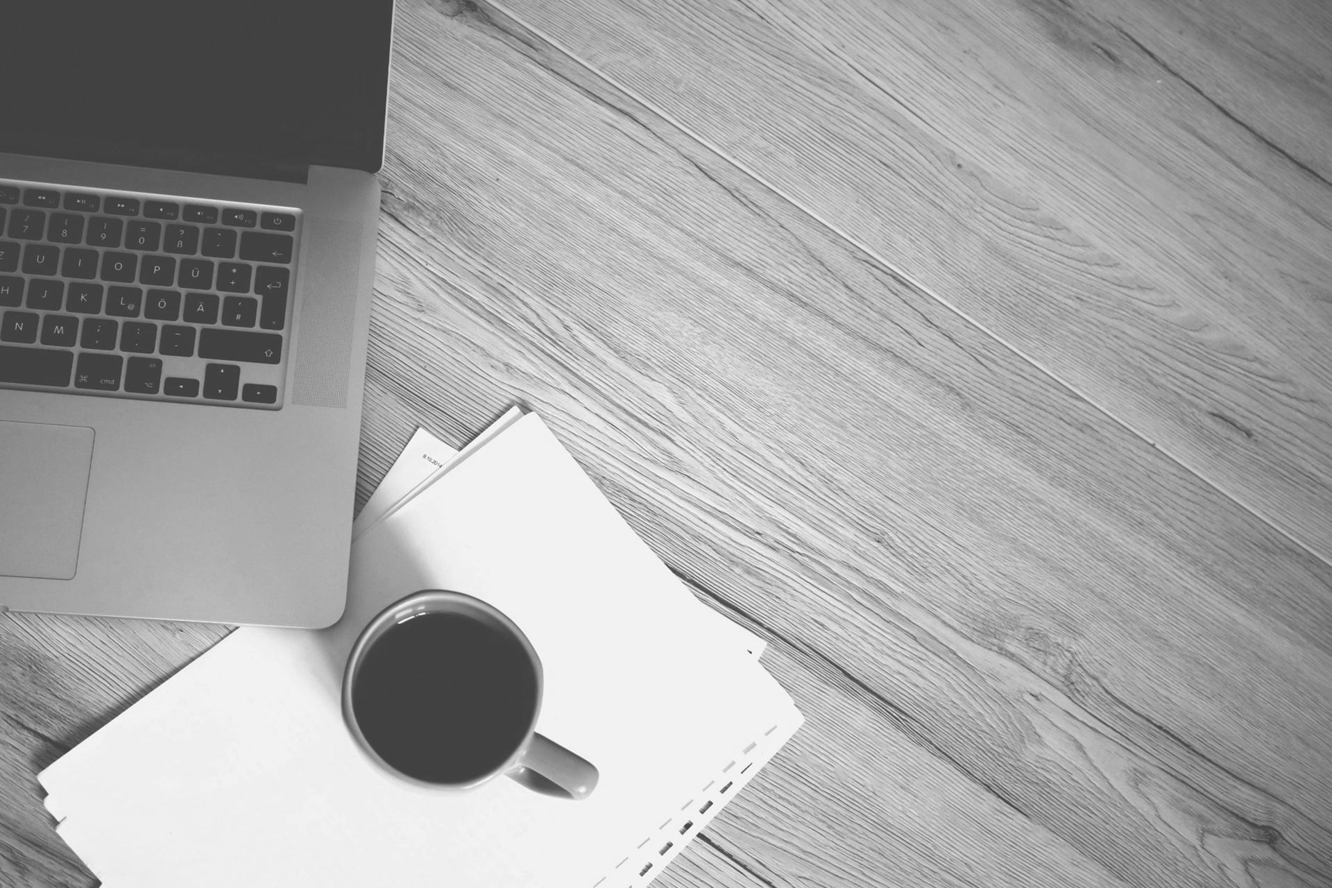 Top-down desk scene with a laptop, coffee cup, and notebook on a textured surface.
