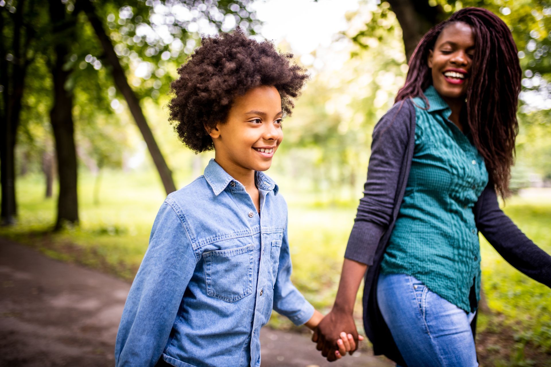 A woman and a boy are holding hands while walking in a park.