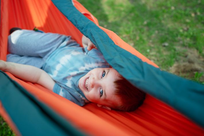 A young boy is laying in a hammock and smiling.