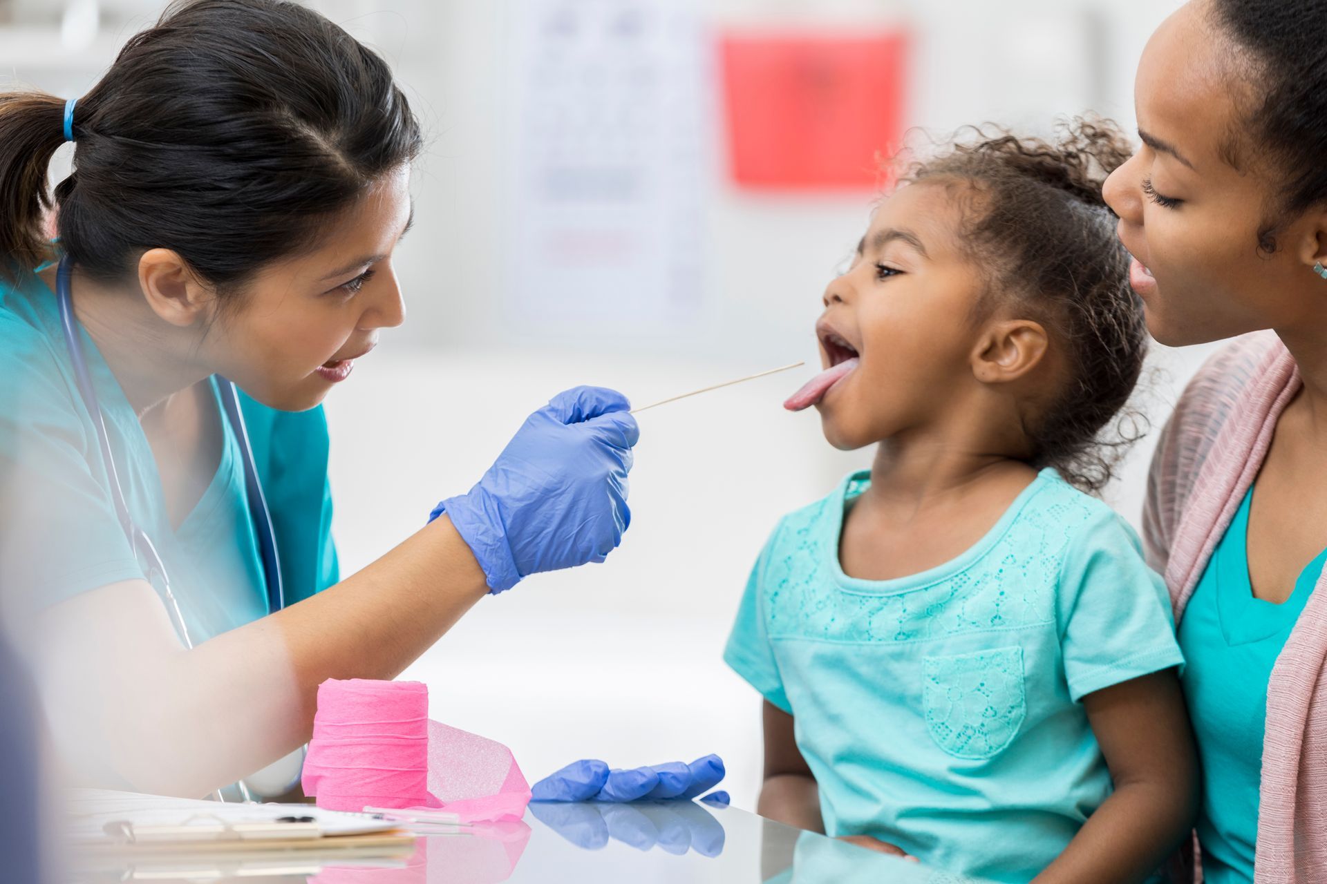 A little girl is getting her throat examined by a doctor.