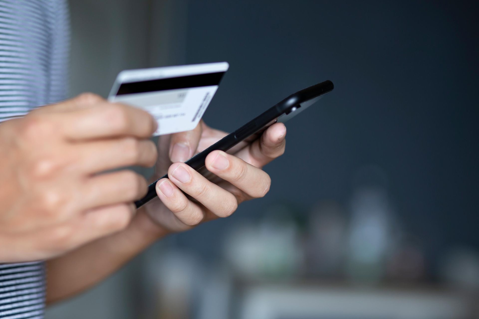 A person is holding a credit card and a cell phone.