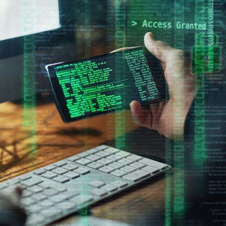A person is holding a cell phone in front of a keyboard that says access granted