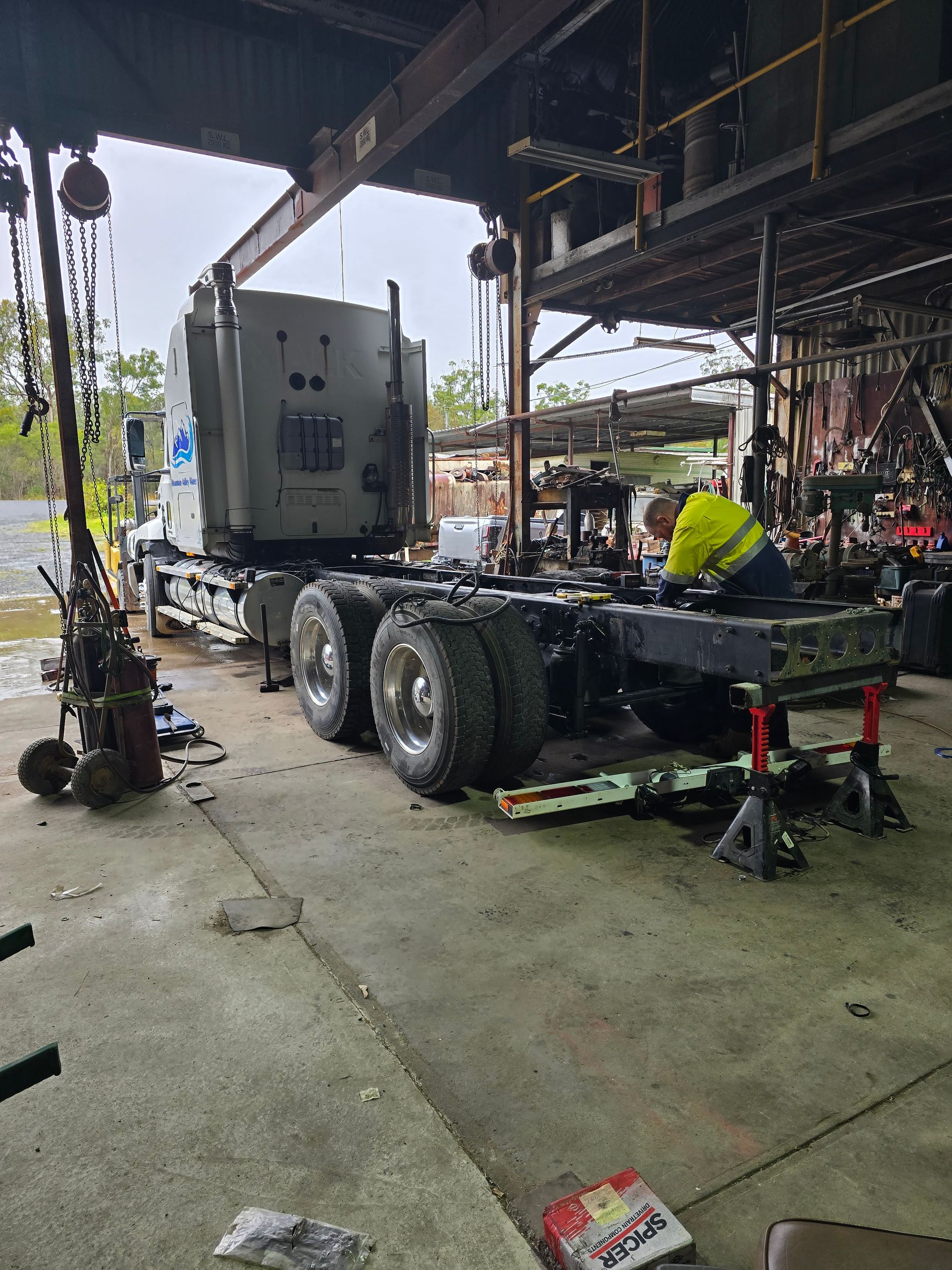 A Person Works on The Chassis of A Grey Semi-Truck Inside an Industrial Garage — Banana Coast Heavy Diesel in Woolgoolga, NSW