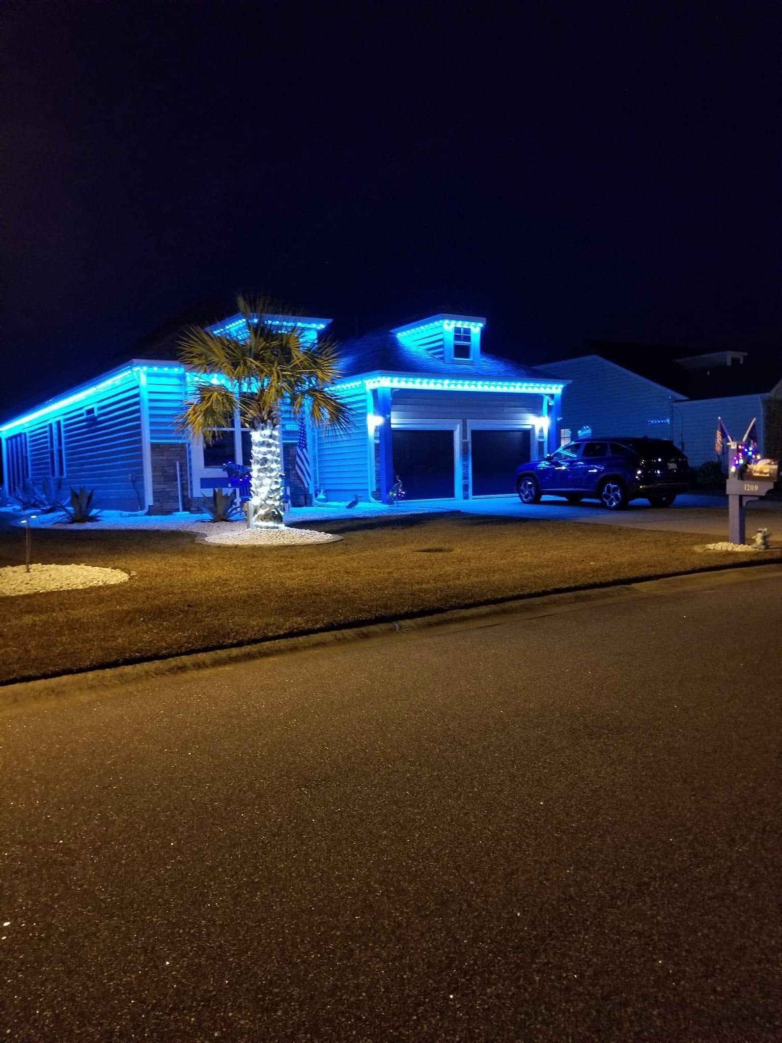 Blue-lit house decorated for the holidays at night, viewed from the street.