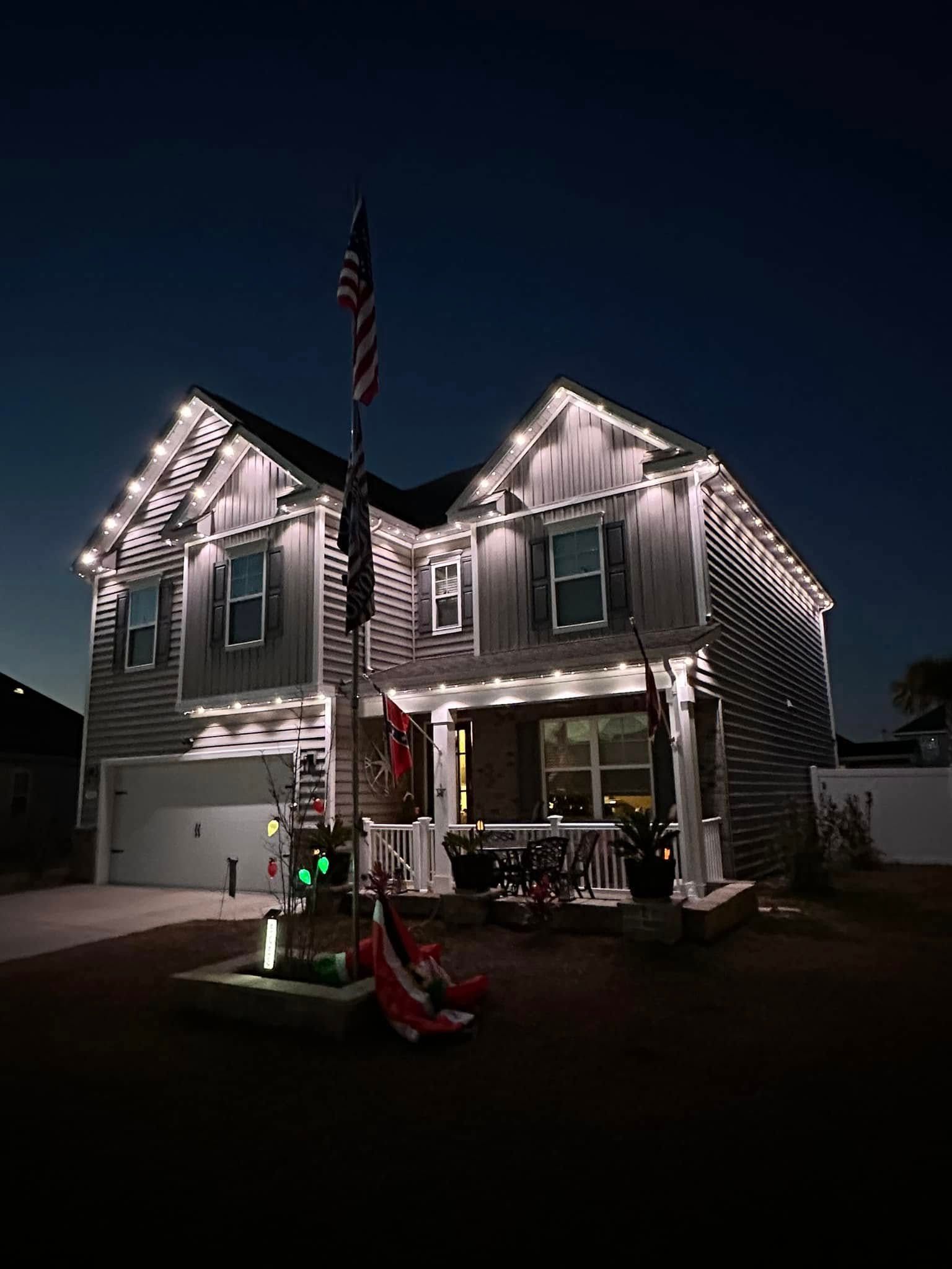 House outlined in white holiday lights at night, with an American flag and decorated front porch
