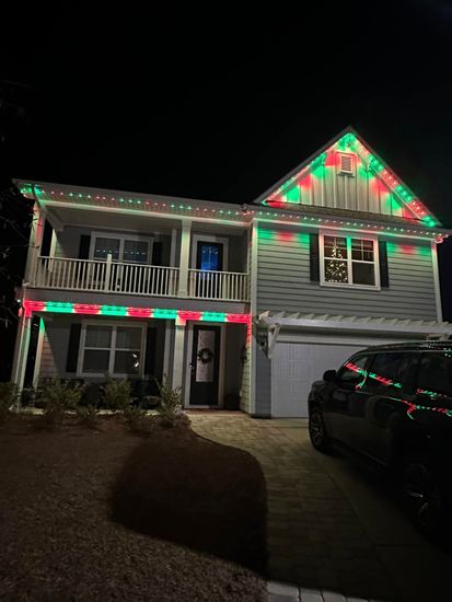 Two-story house at night with red and green holiday lights and a parked black SUV in the driveway