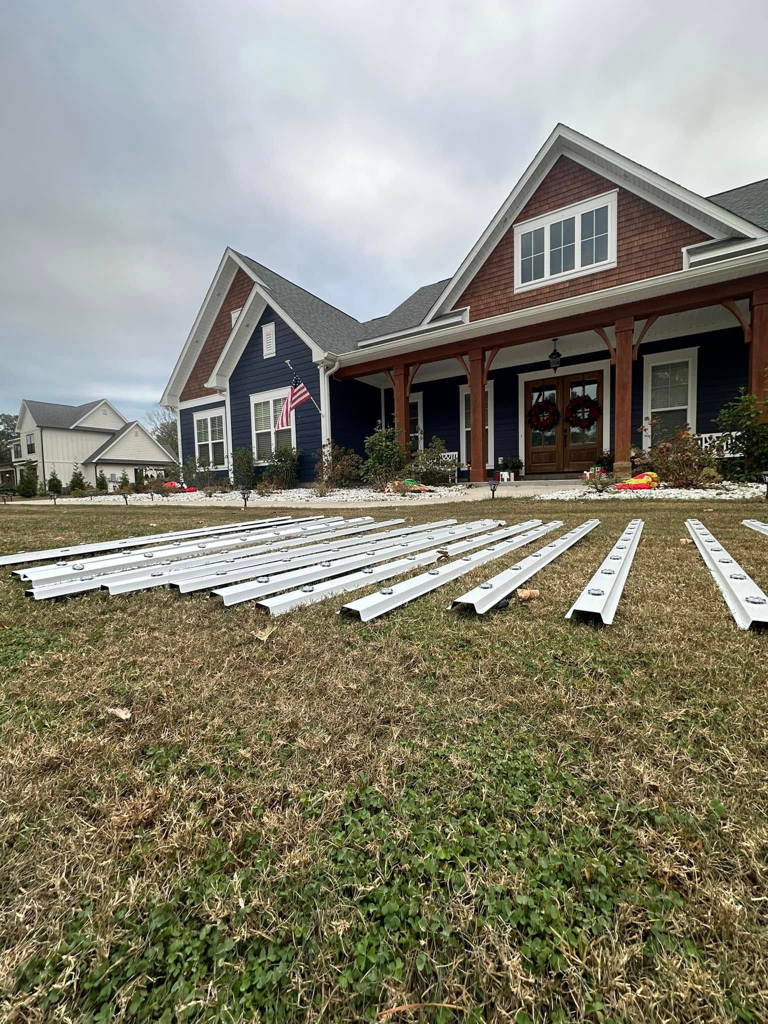 Red house with a porch and white gutter pieces laid out on the lawn under a cloudy sky.