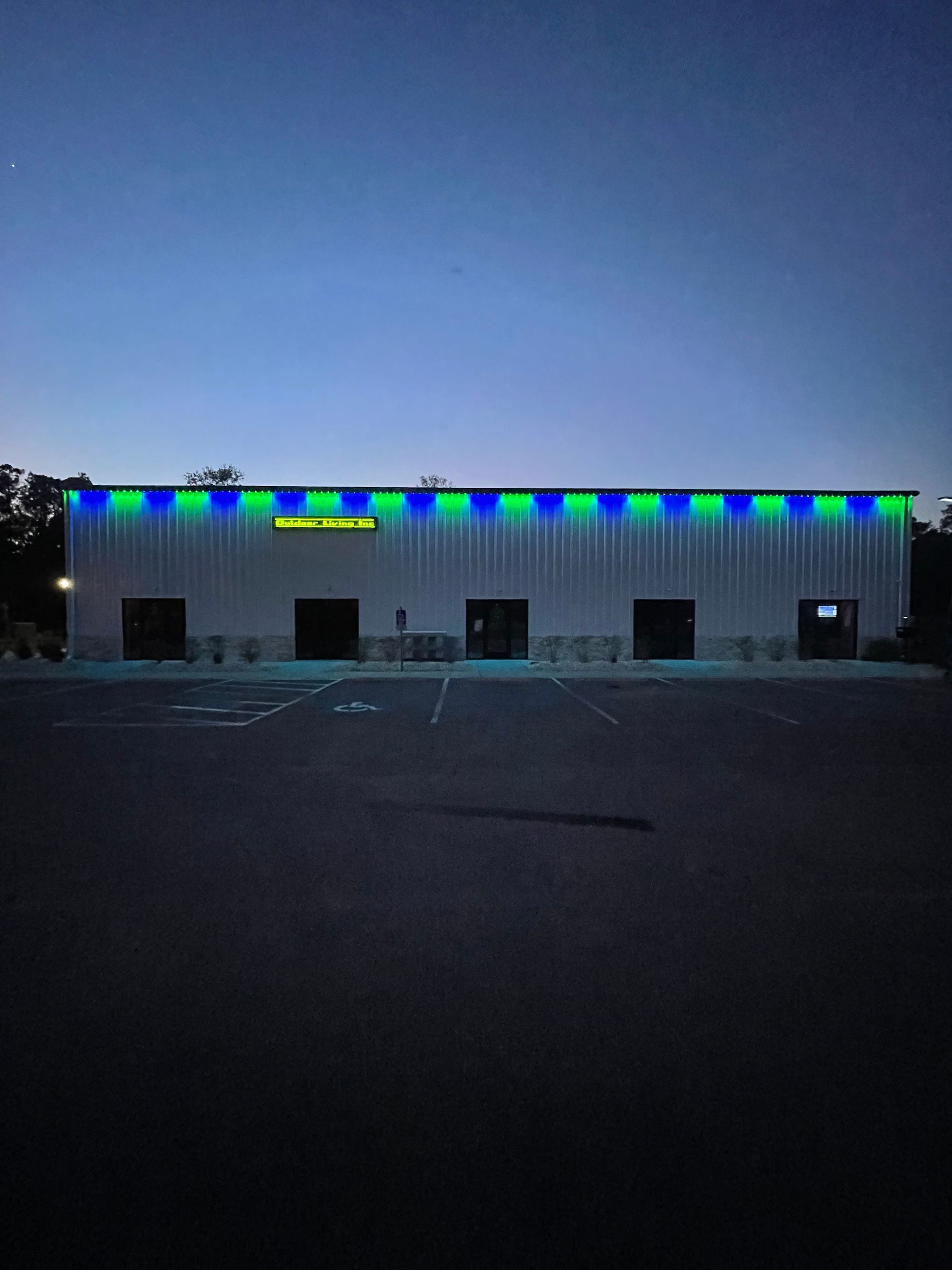 Low building at dusk with blue-green lights along the roofline and dark parking lot in front