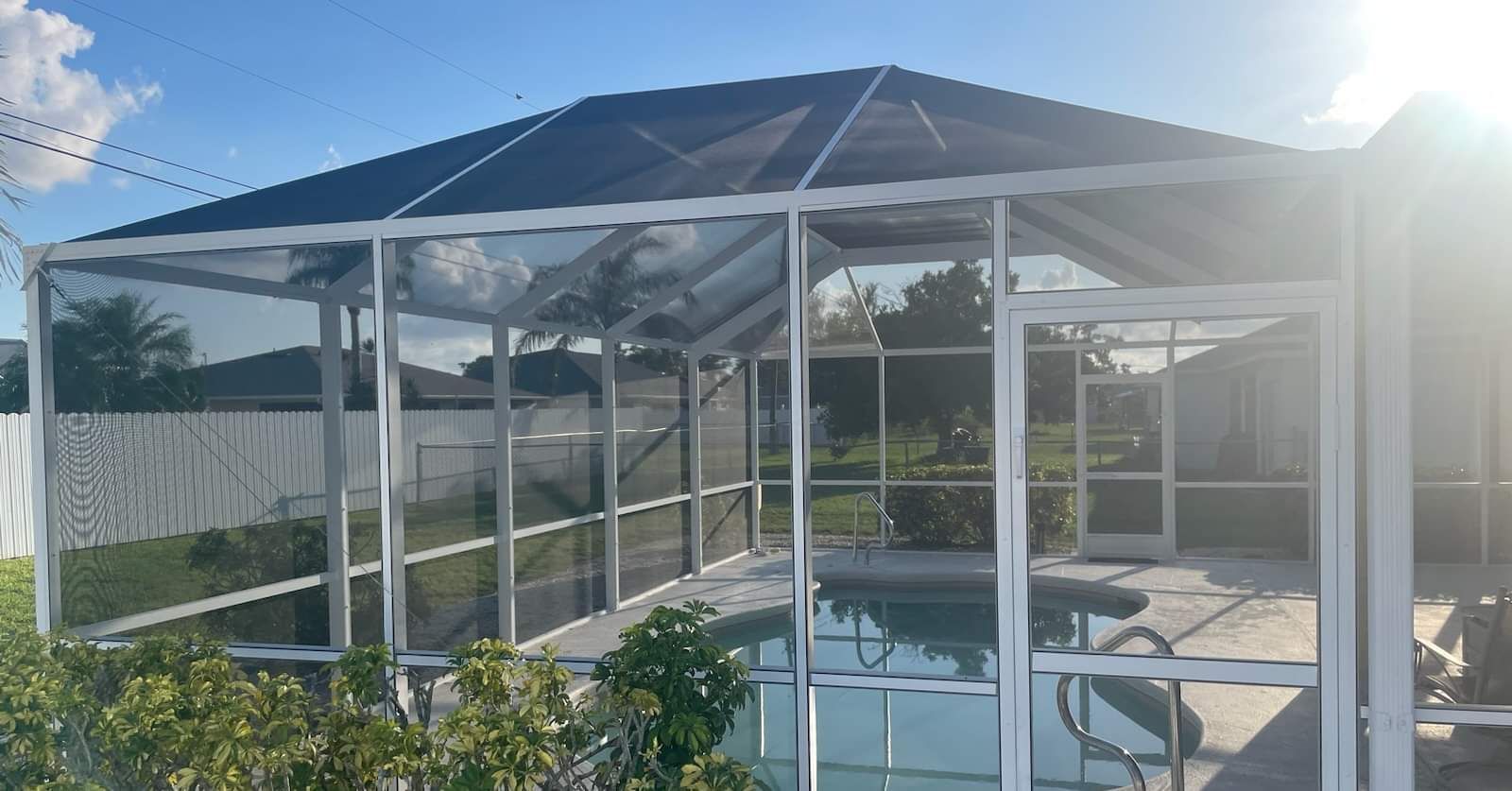 There is a large swimming pool in the backyard of a house with a screened in area.