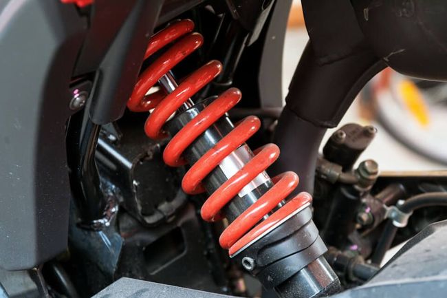Red coil-over shock absorber on a motorcycle, mounted on a black frame.