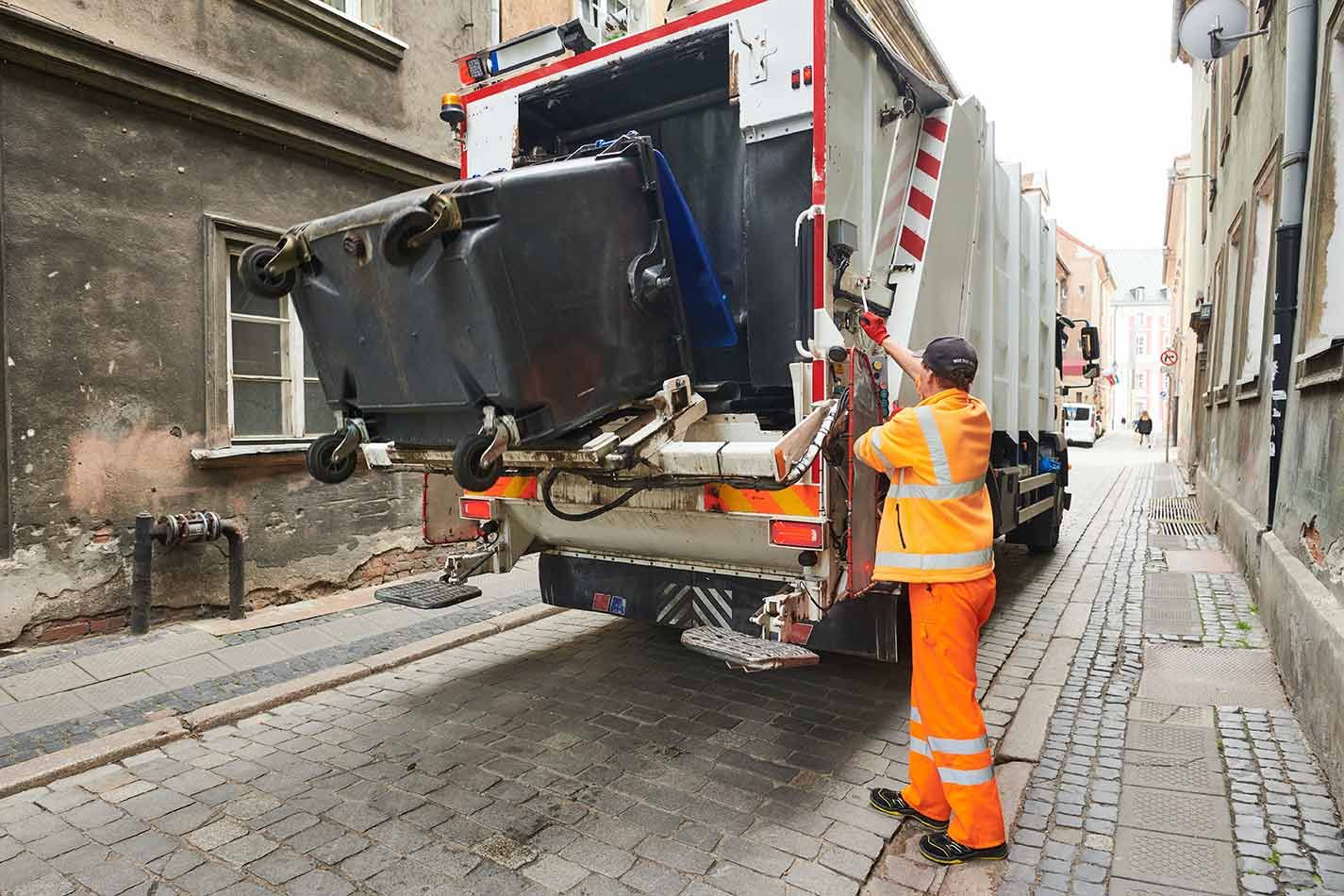 A Man is Loading Garbage Into a Garbage Truck on a City Street — Truck Training and Assessments In Umina Beach, NSW