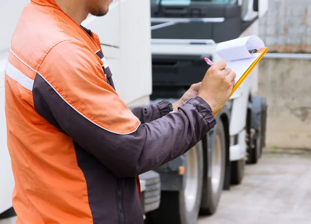 A Man is Writing on a Clipboard in Front of a Truck — Truck Training and Assessments In Umina Beach, NSW