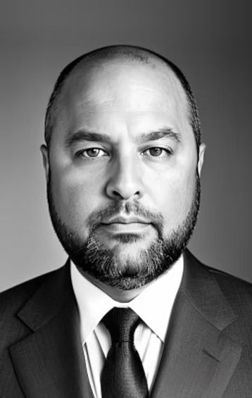 Black-and-white headshot of a bald man in a suit and tie, looking directly at the camera.