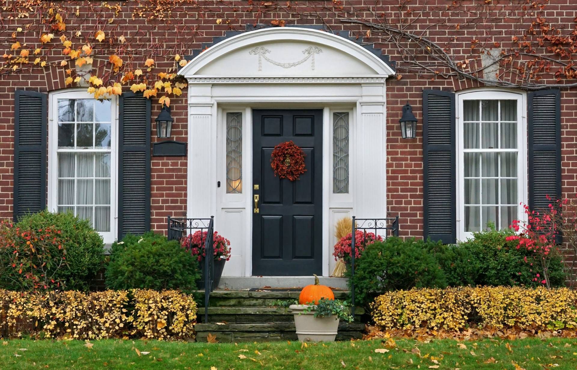 A brand new black front door with gold hardware and a fall wreath on the door