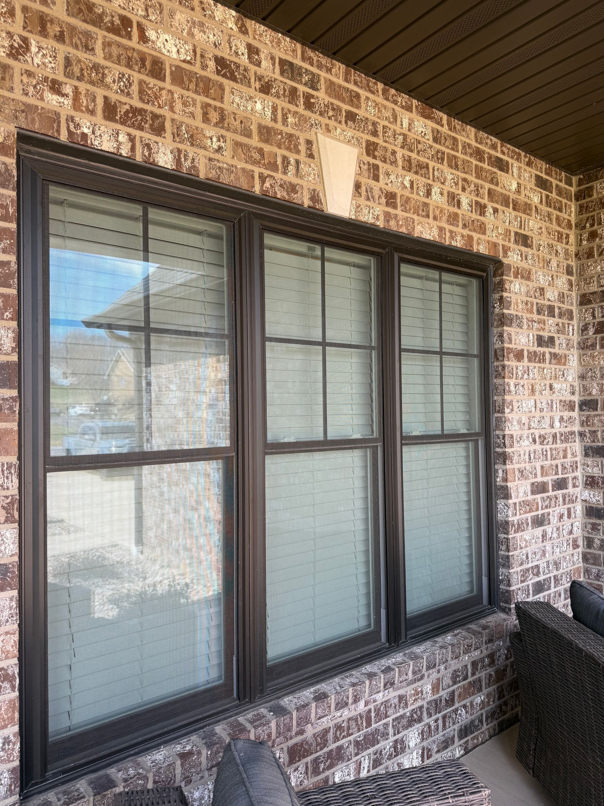 A dark-framed triple-pane window with grid patterns on a brown brick exterior wall.