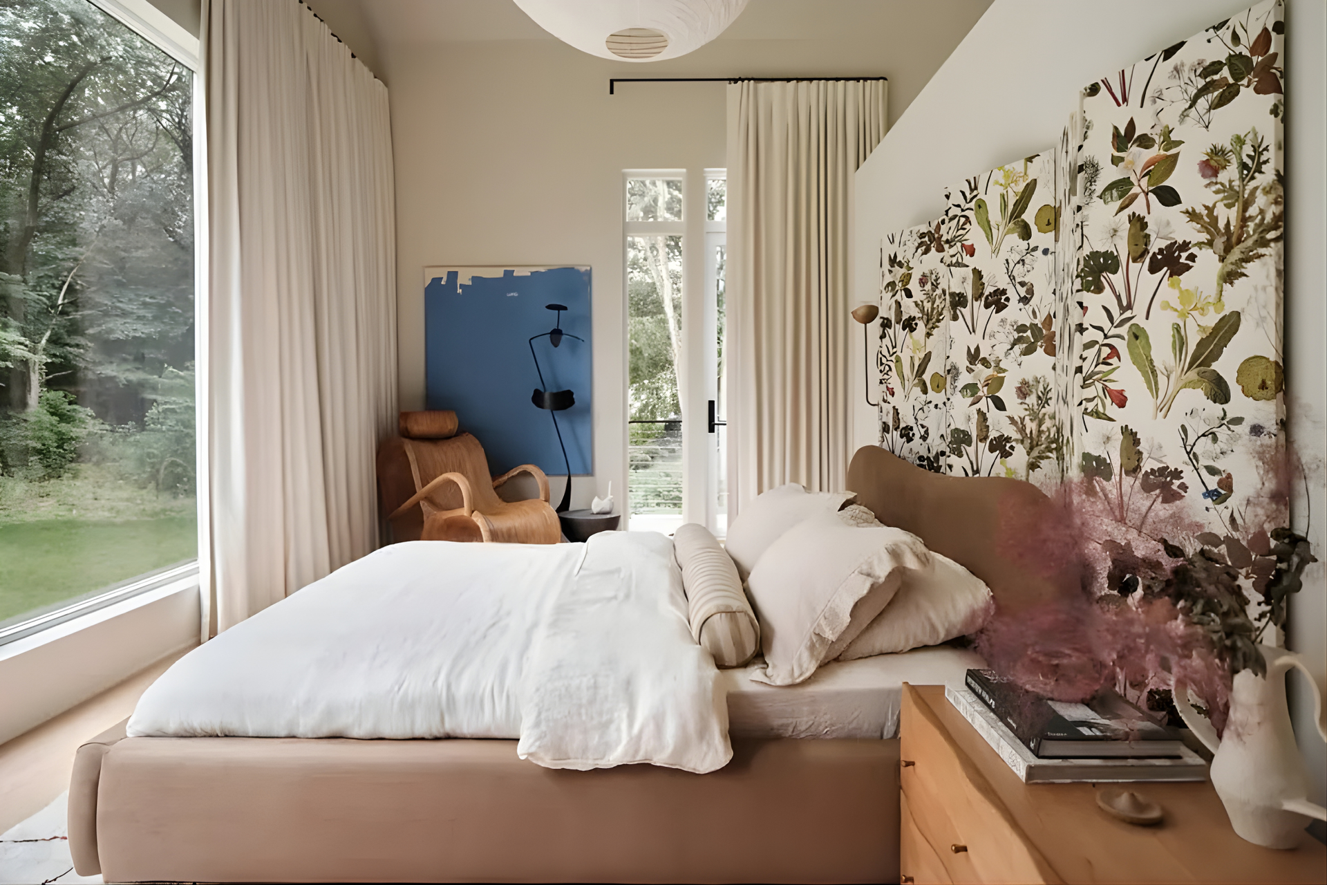 A modern bedroom with a floral headboard, white bedding, tan platform bed, and floor-to-ceiling windows with beige curtains.