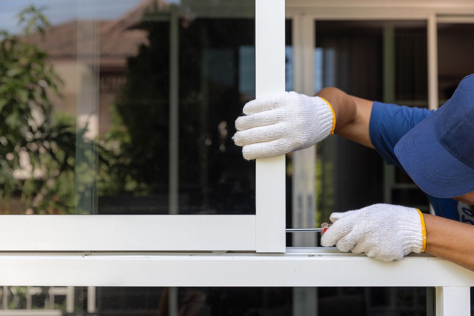 A professional wearing gloves and using tools to install a replacement window in a residential home