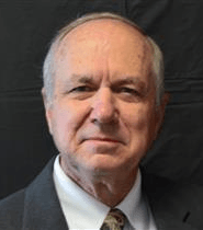 An older man with graying hair, wearing a suit jacket, looking directly at the camera.