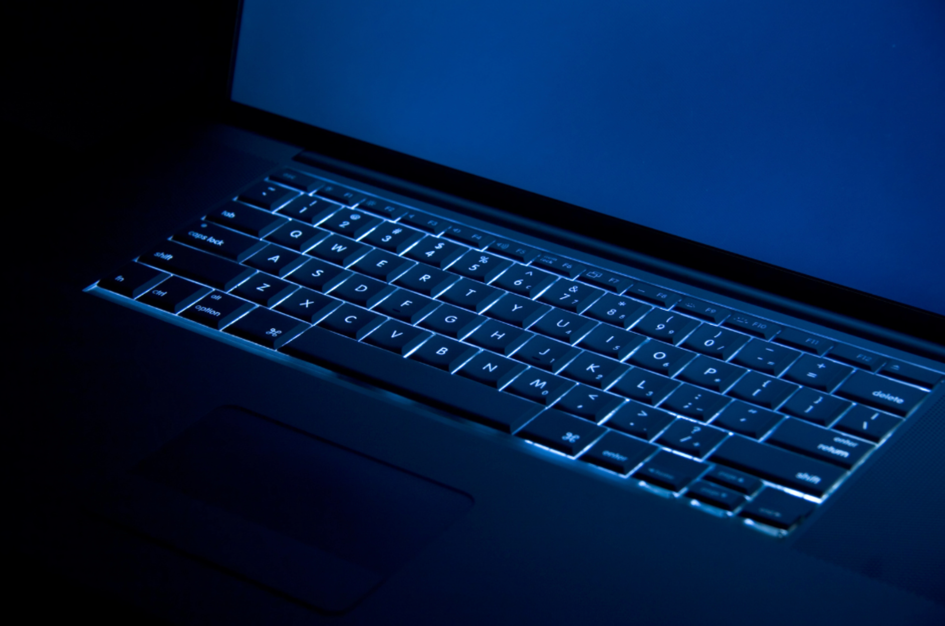 The keyboard of a laptop is lit up in the dark