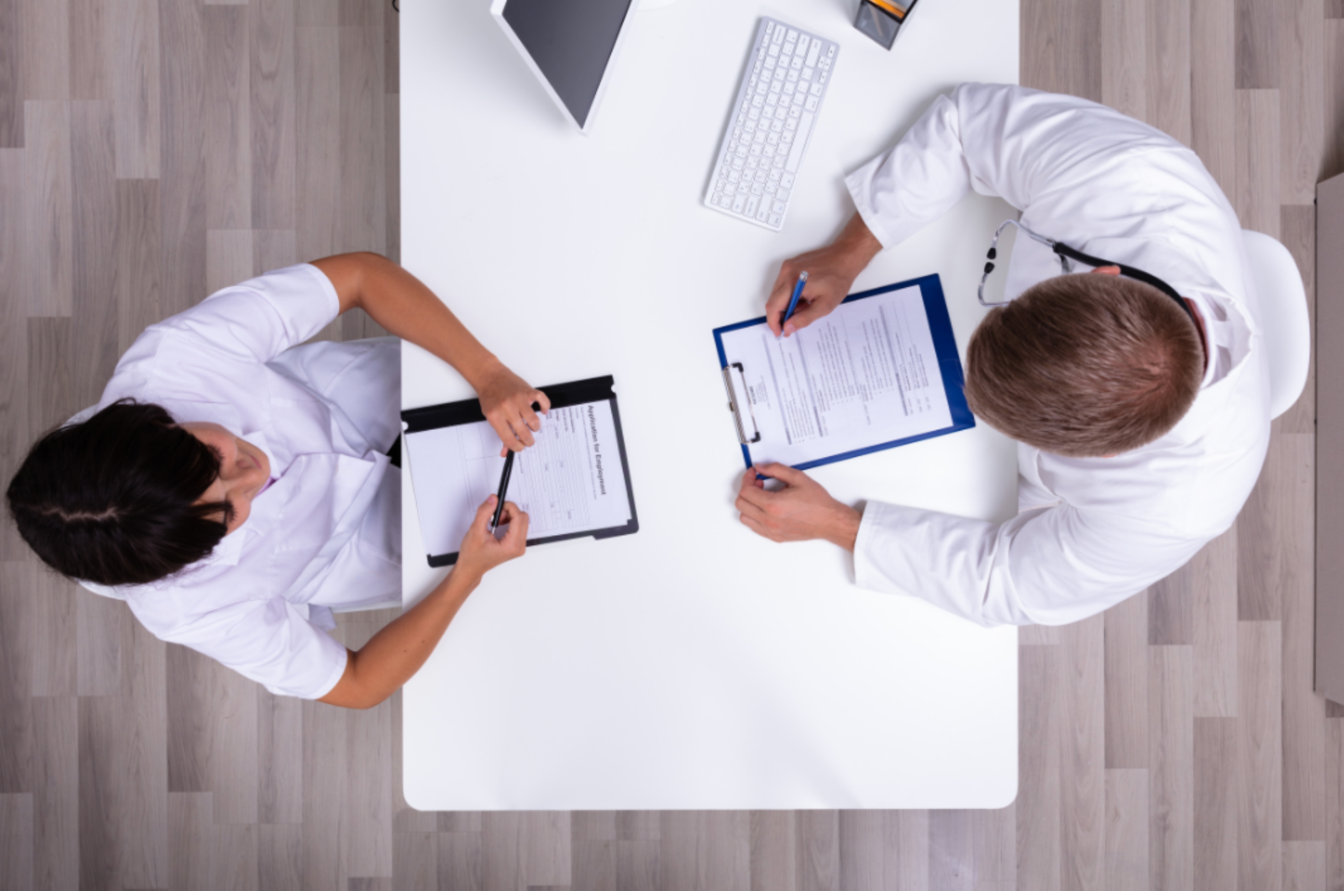 A doctor and a nurse are sitting at a table writing on clipboards.