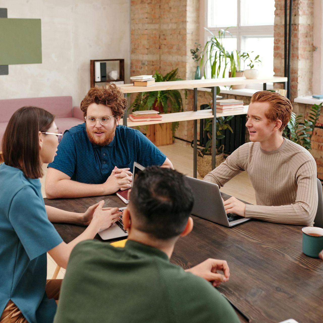 A group of people are sitting around a table with laptops.