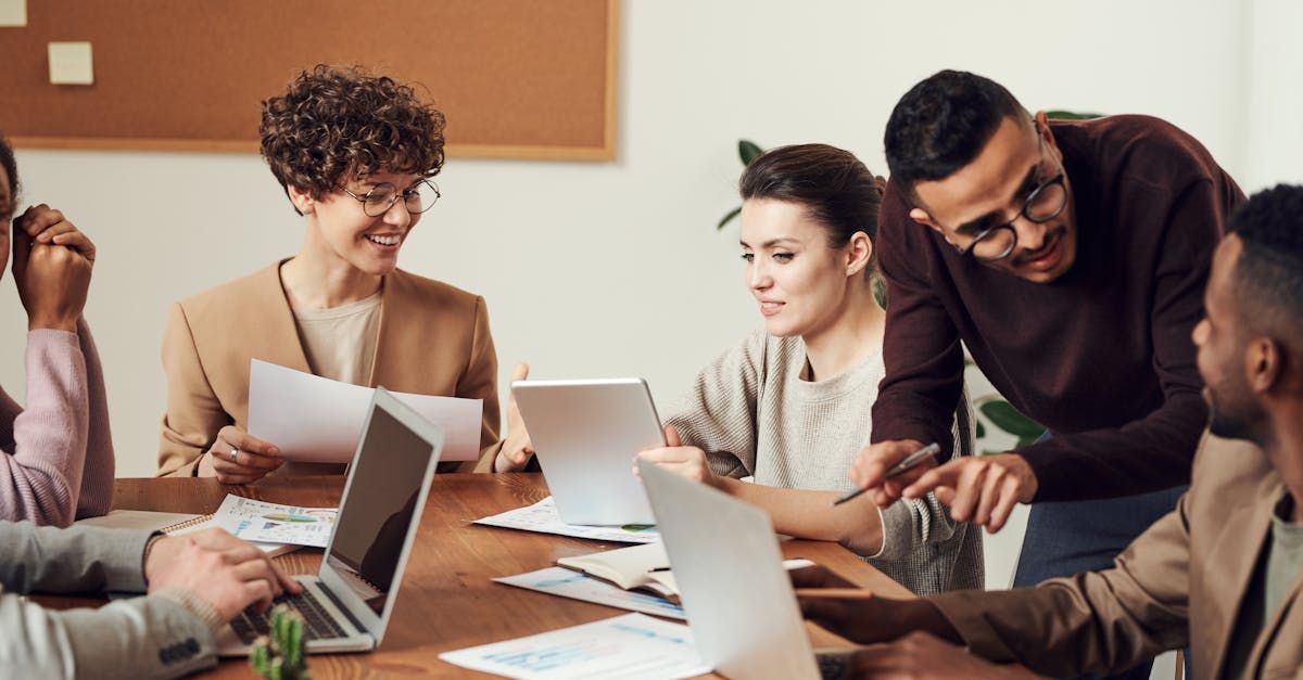 A group of people are sitting around a table with laptops.