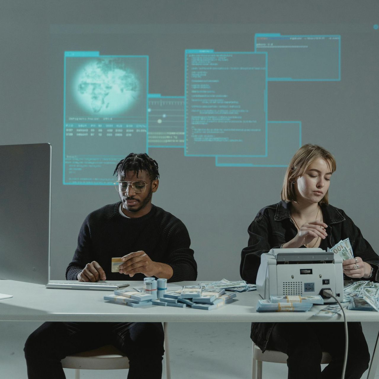 A man and a woman are sitting at a table in front of a computer.