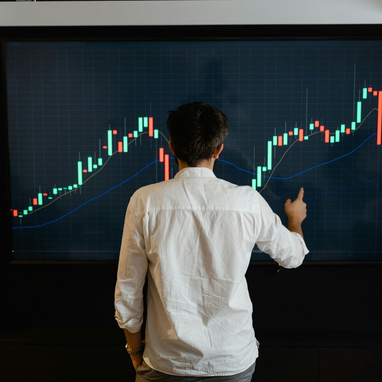 A man is pointing at a graph on a large screen.