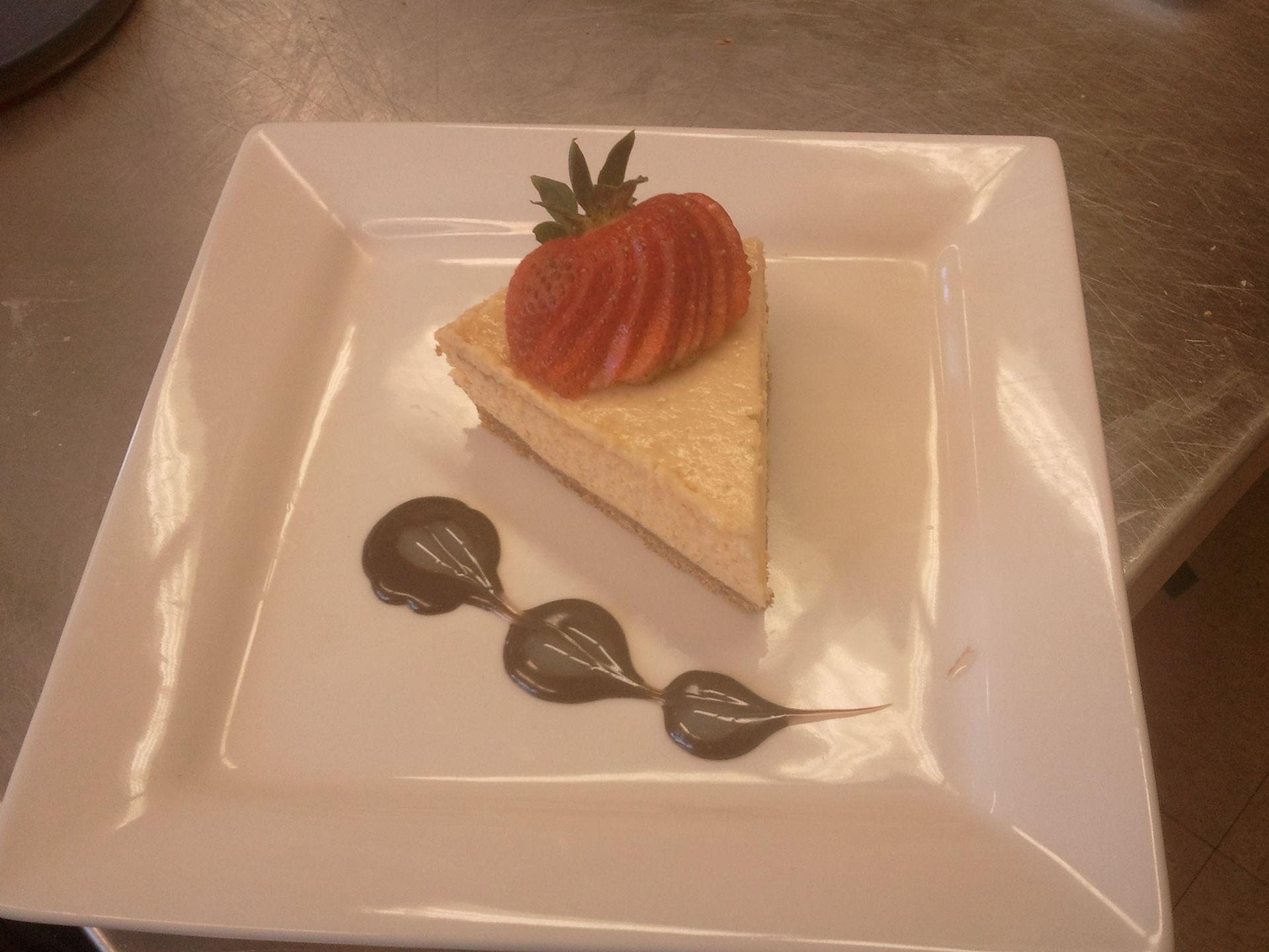 Slice of strawberry cheesecake on a square white plate with chocolate sauce drizzled beside it