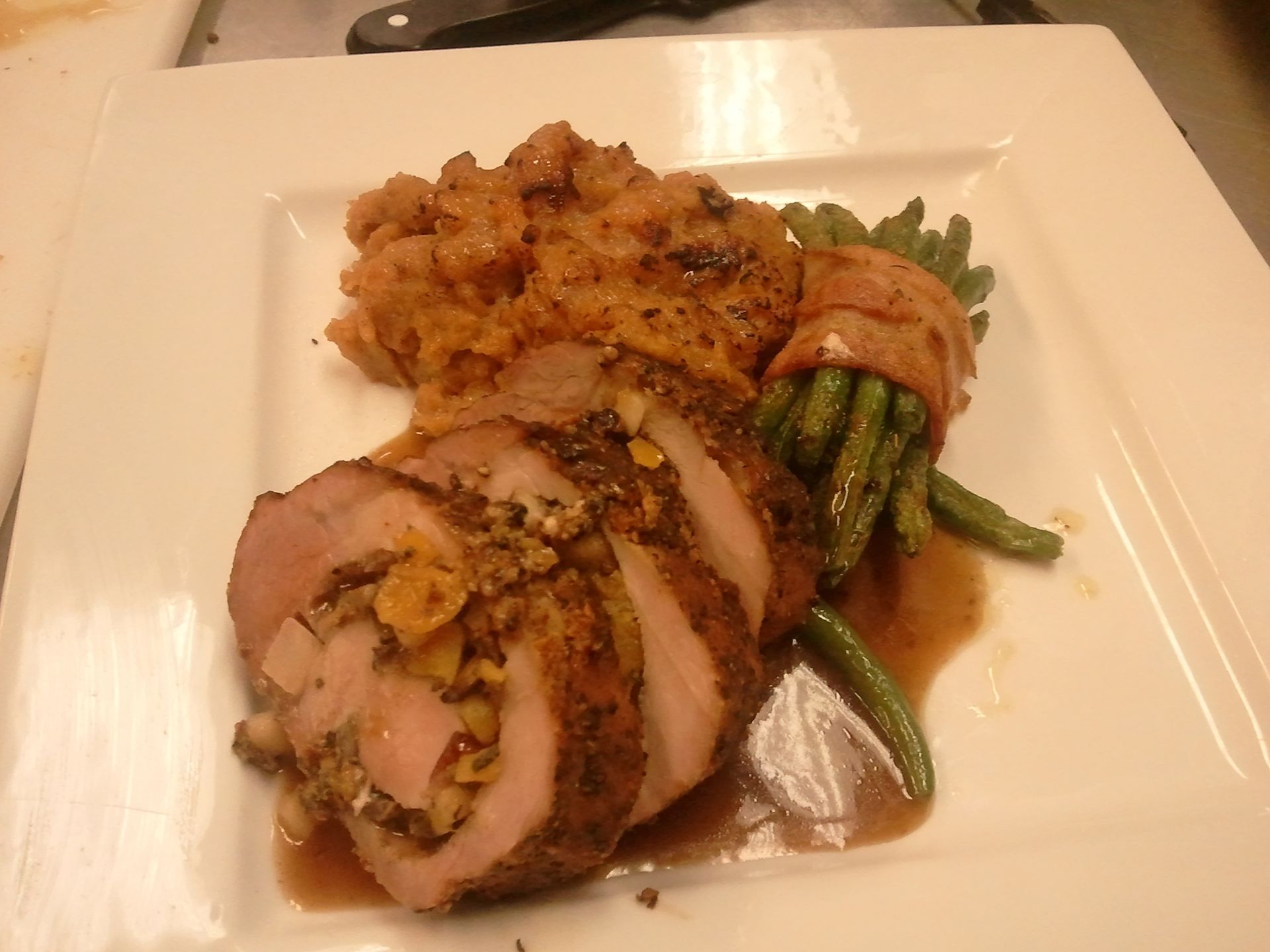 Plated roasted meat slices with sauce, asparagus, and mashed potatoes on a white square plate