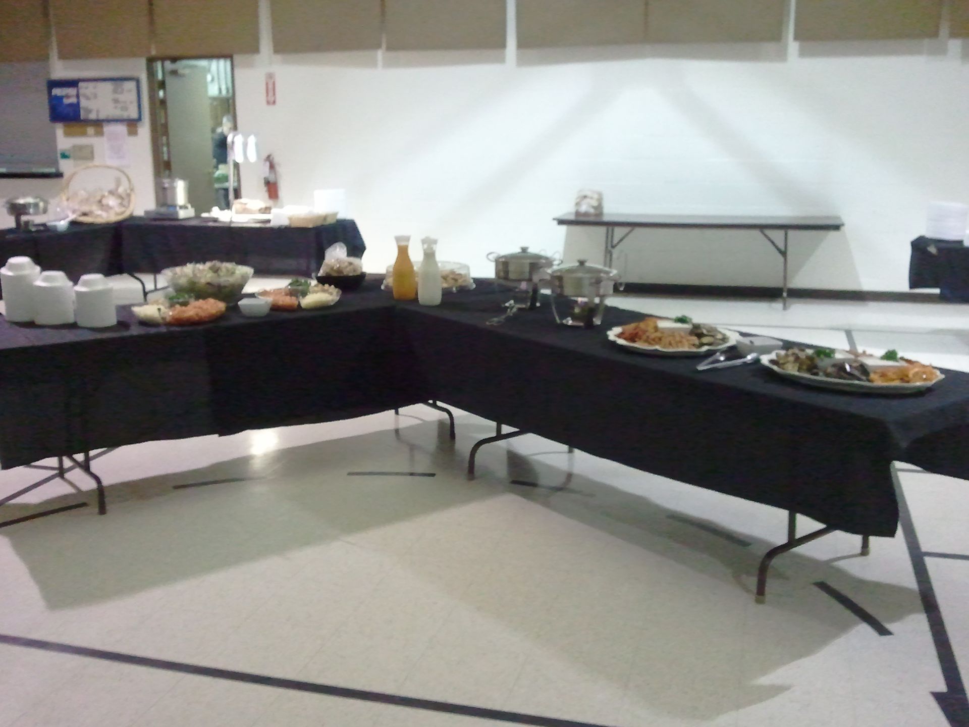 Conference room buffet table with black tablecloths, plates of food, drinks, and serving trays.