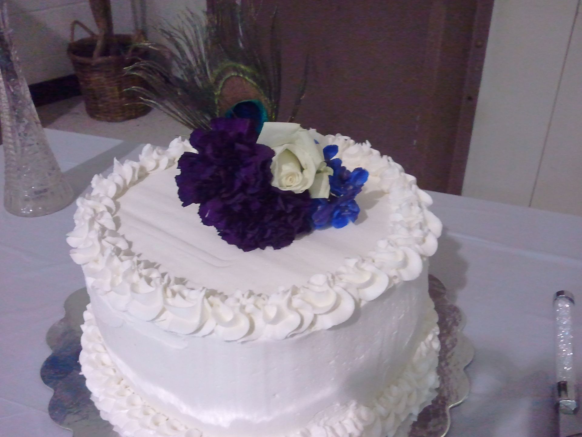 White frosted cake with purple and white flowers on top, sitting on a table