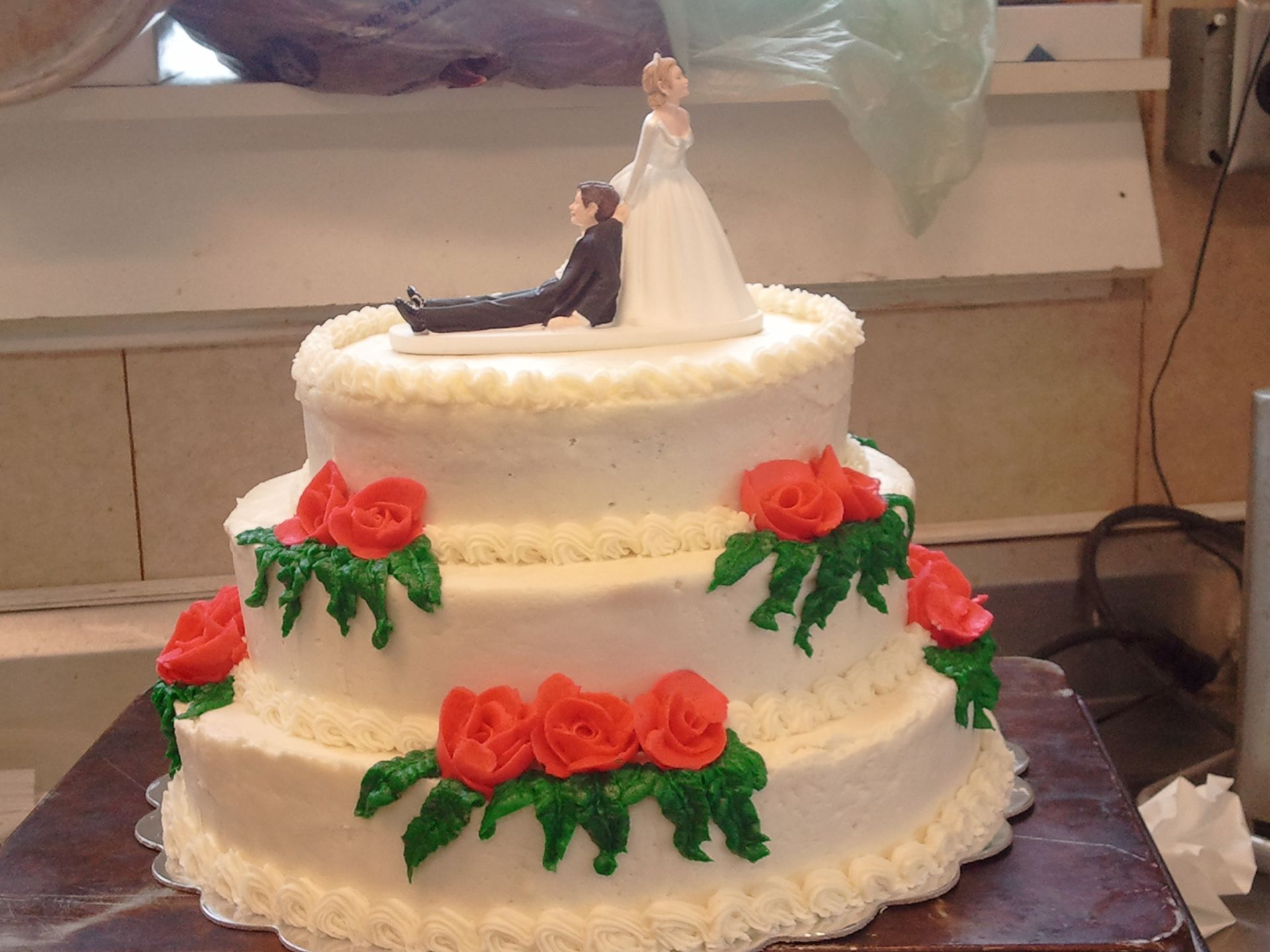 Three-tier white wedding cake with red roses and bride-and-groom topper