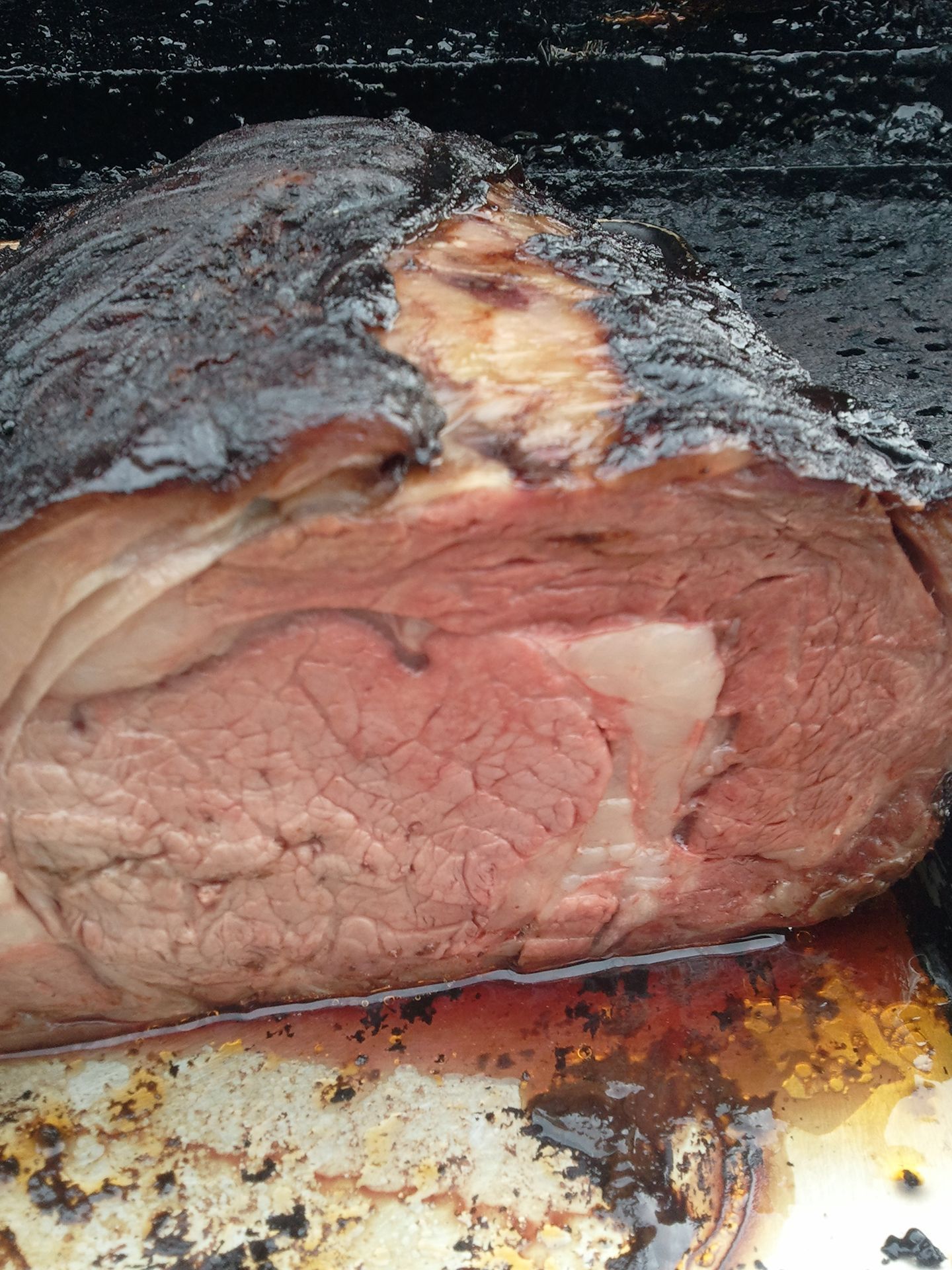 Close-up of a sliced smoked roast with a dark crust, showing pink meat on a metal tray