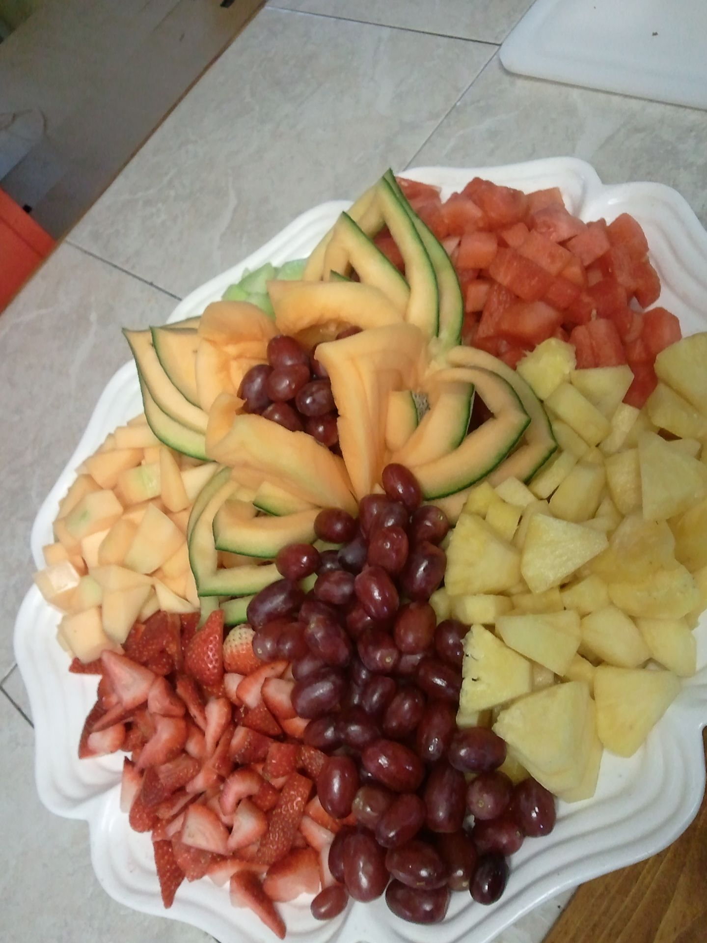 Platter of assorted fresh fruit slices, including grapes, melon, pineapple, strawberries, and watermelon.
